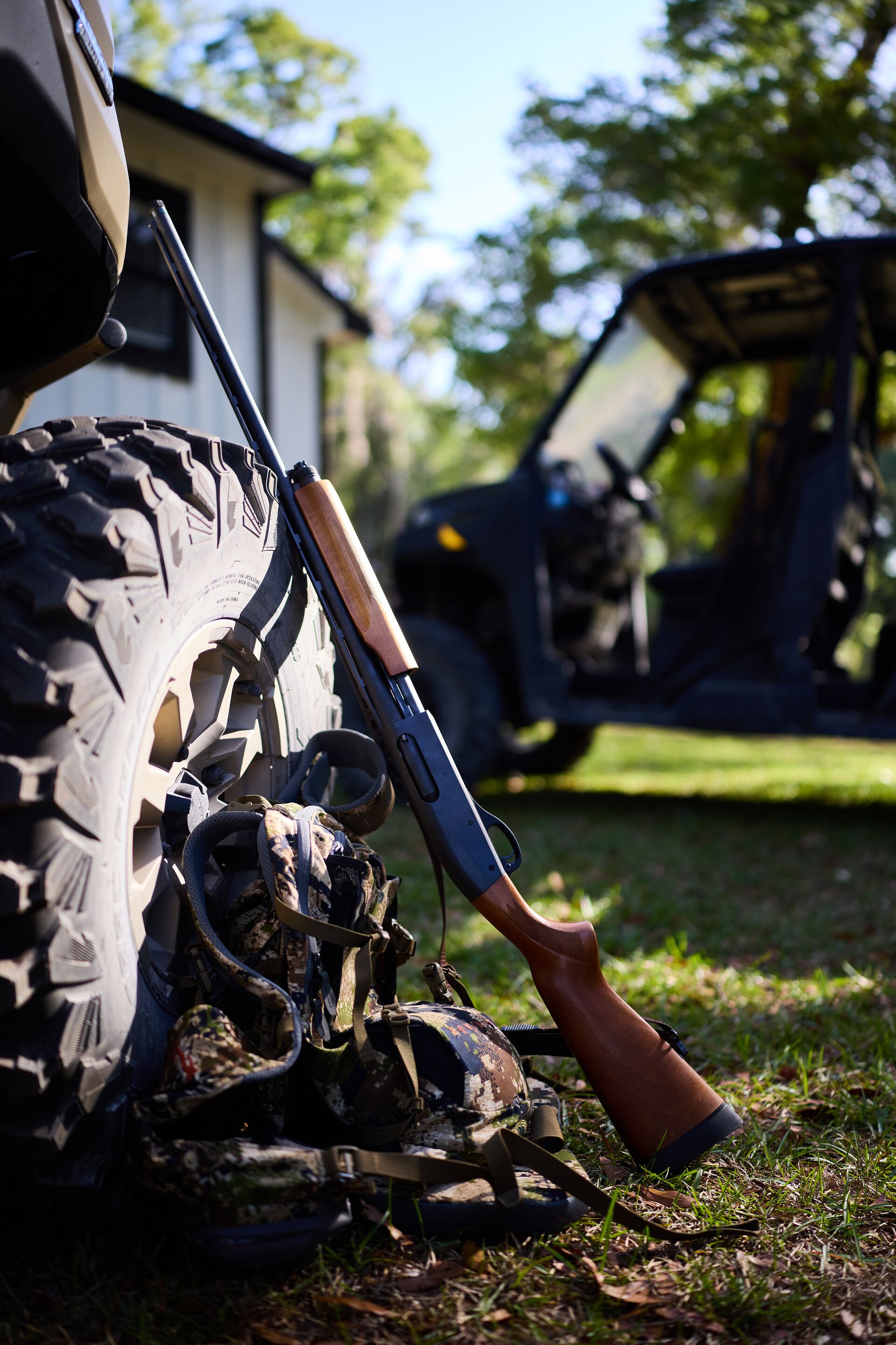 Shotgun and hunting gear leans against truck tire, turkey hunting concept.