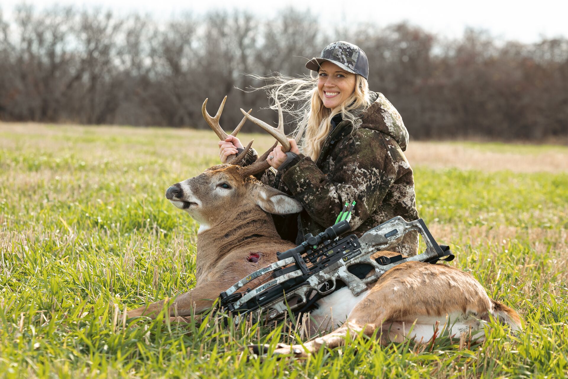 Smiling woman with buck deer on the ground after hunt, shot placement concept.