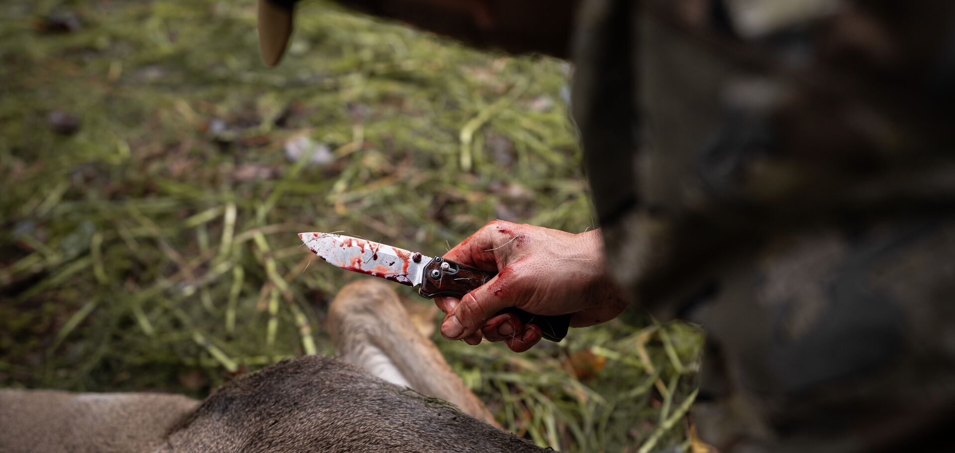 Hunter with knife near animal after hunt, venison concept.