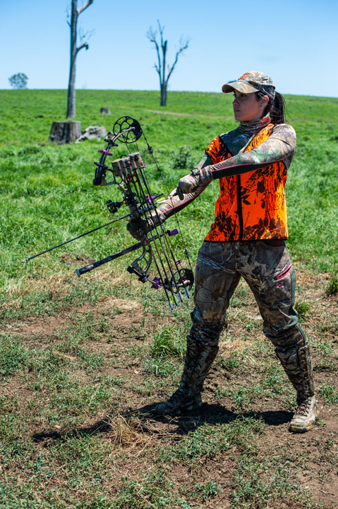 A female hunter in blaze orange draws a bow, Georgia hog hunting season concept. 