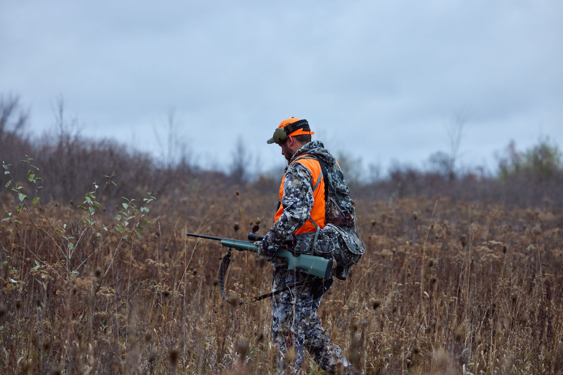 Hunter in blaze orange and camo with rifle in field, wild hog hunting in Alabama concept. 
