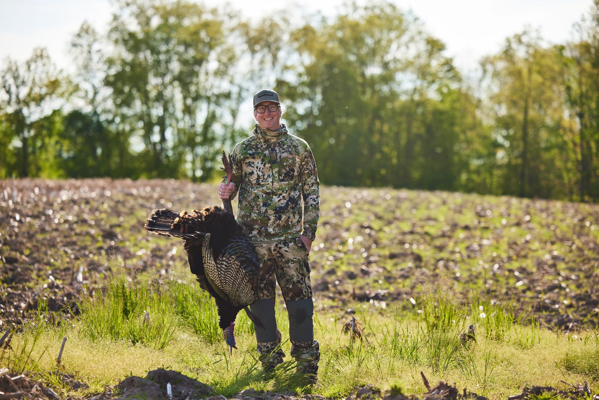 Hunter in camo holds up a turkey after a hunt.