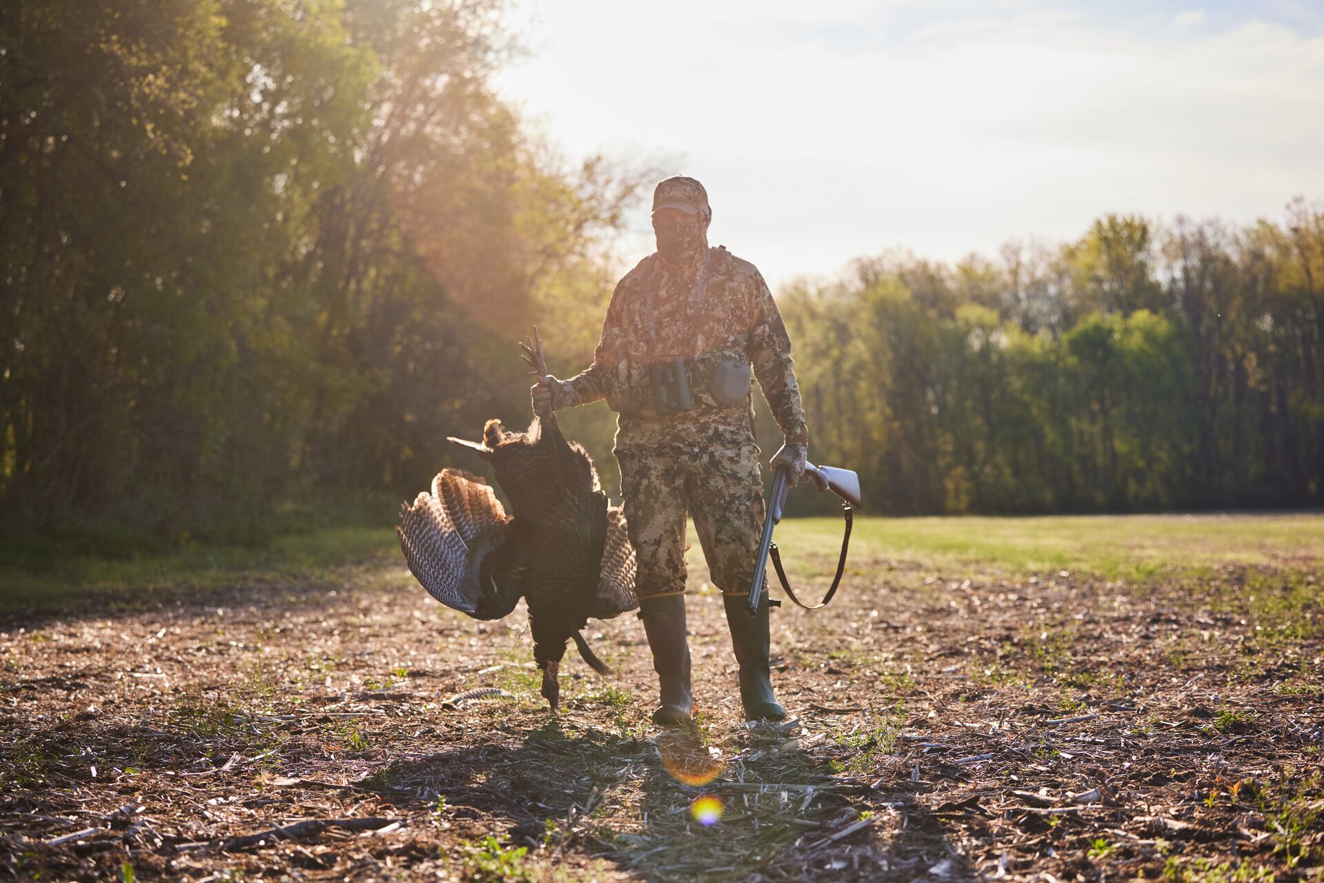 A hunter holds up a turkey with the sun behind them, afternoon turkey hunting concept. 