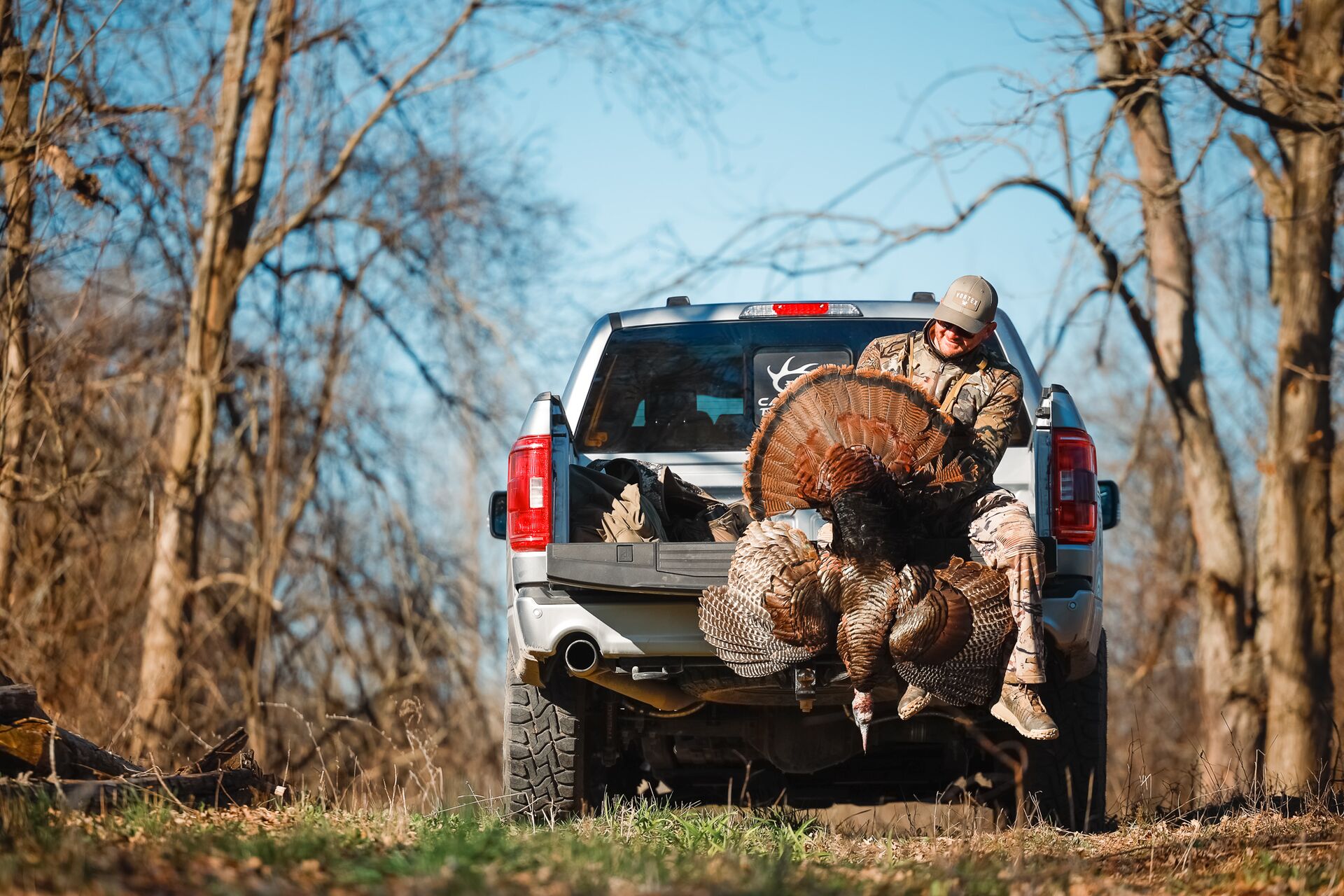 Hunter sitting on a truck tailgate showing a turkey after a hunt. 