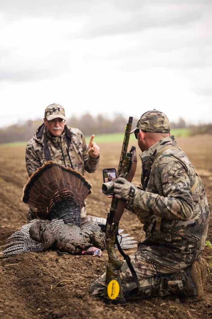 Hunter takes a photo of another hunter with a turkey after a hunt, spring hunting seasons concept.