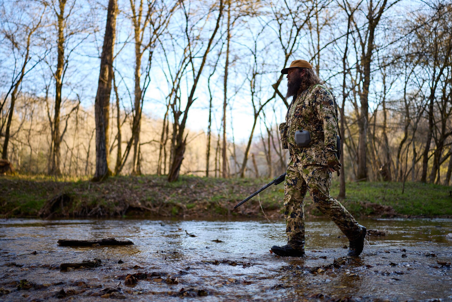 A turkey hunter walks through a creek in the woods, spring turkey hunting tactics concept. 