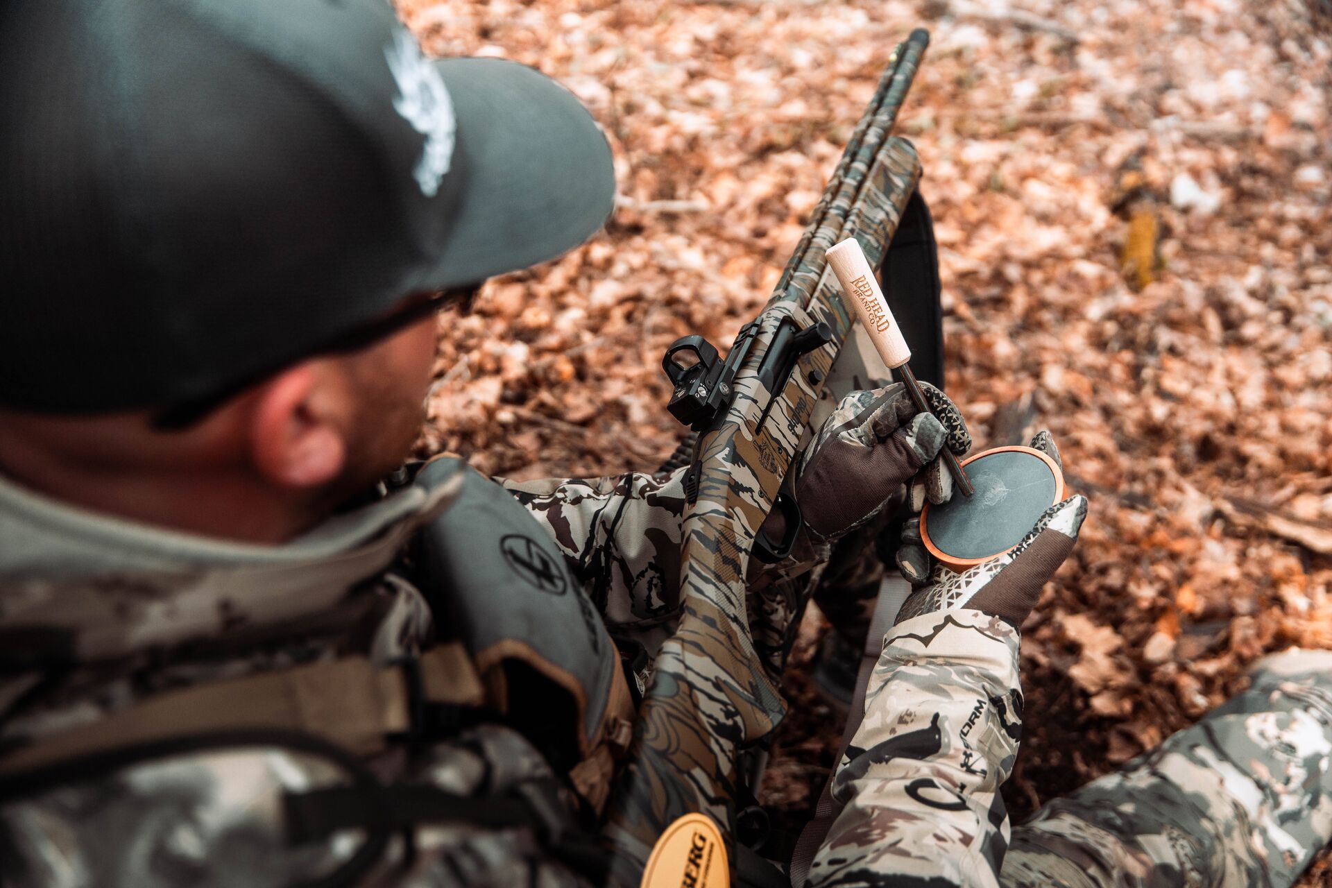 A hunter sits in the woods using a turkey pot call. 