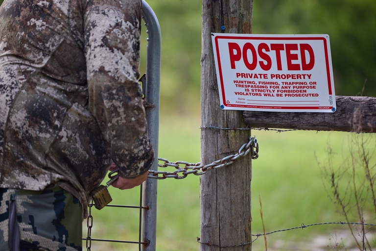 A hunter next to a fence with private property sign, how to get landowner permission to hunt pennsylvania concept.