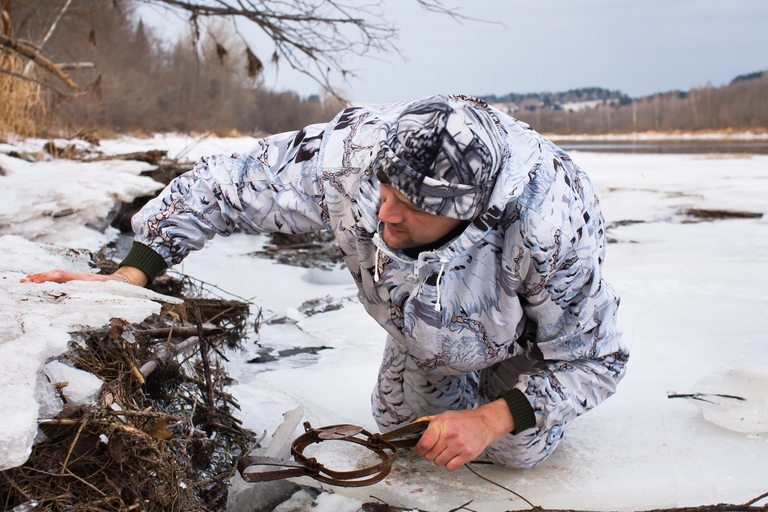A hunter sets a trap in the snow, hunting and trapping regulations concept. 
