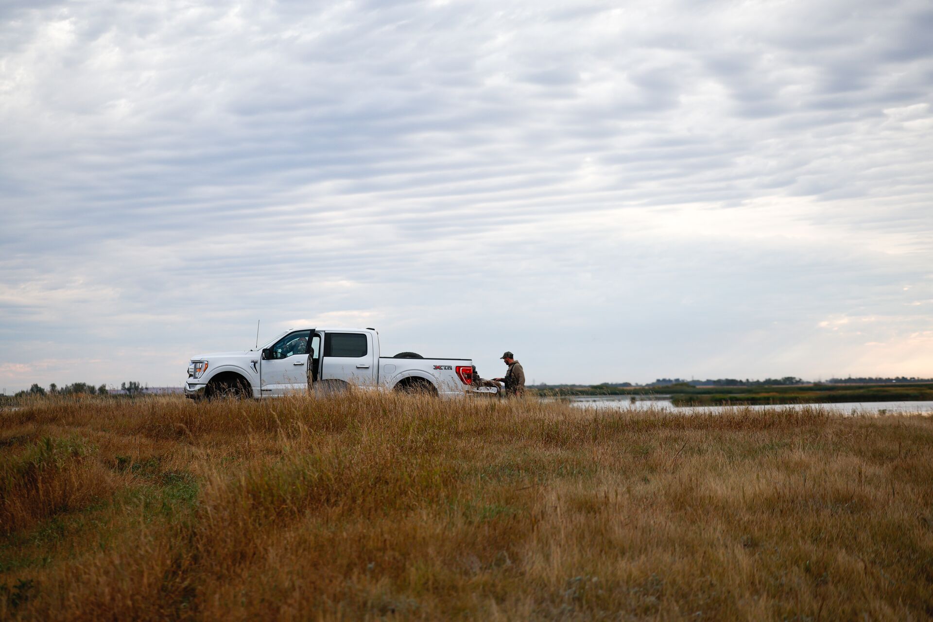Hunter stands behind open truck bed, leasing land for hunting concept.
