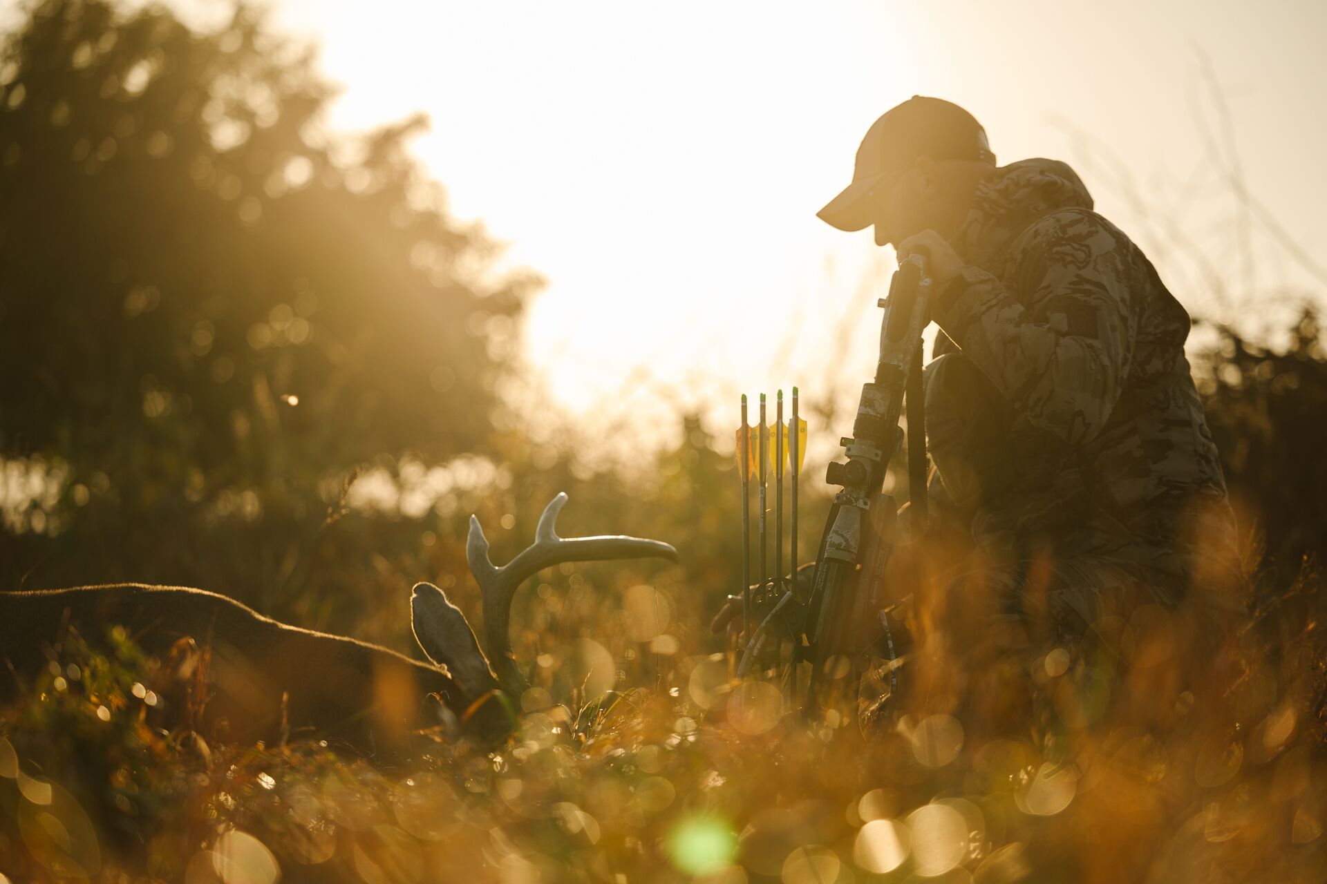 Hunter with bow kneeling next to deer on the ground.
