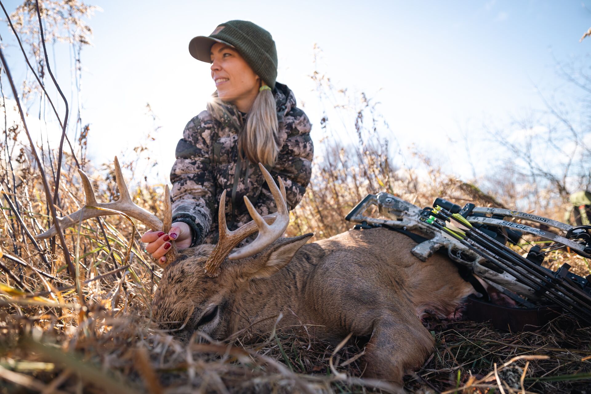 Woman hunter sits with deer and bow after shot, field dressing a deer concept.