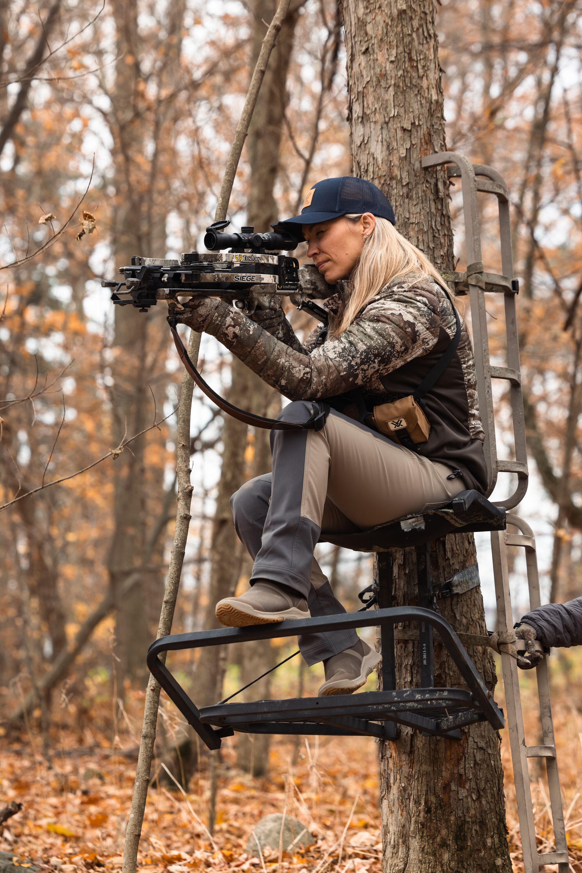 Woman aims crossbow in tree stand, Louisiana bowhunter concept. 