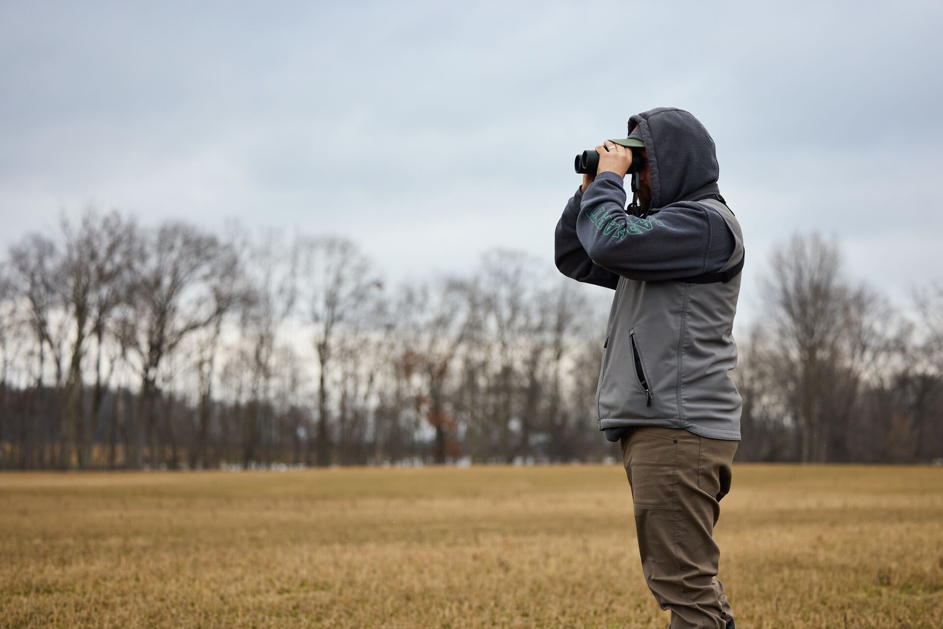 Hunter using binoculars in a field to scout for deer. 