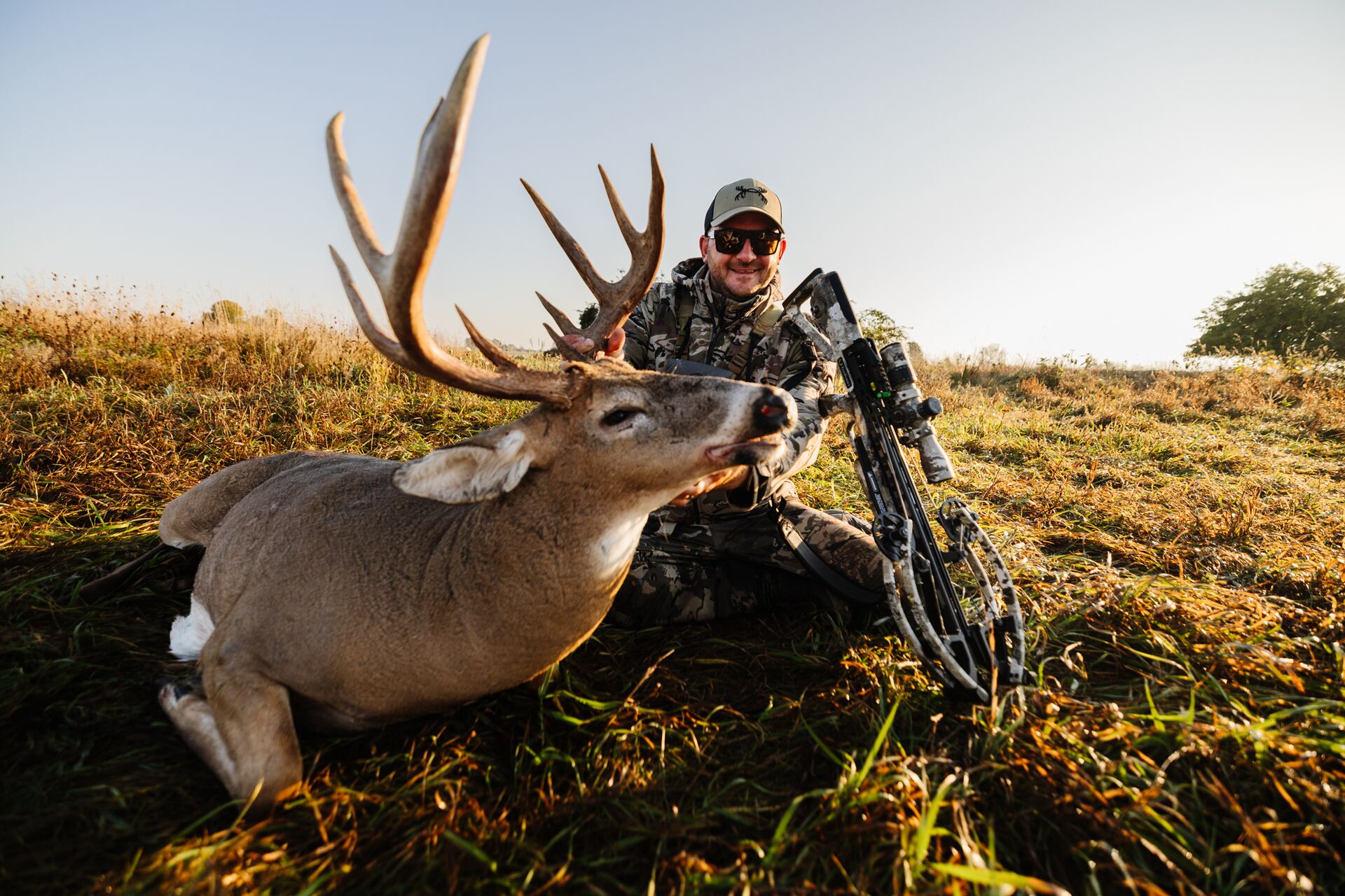Hunter smiling with deer on the ground after hunt.