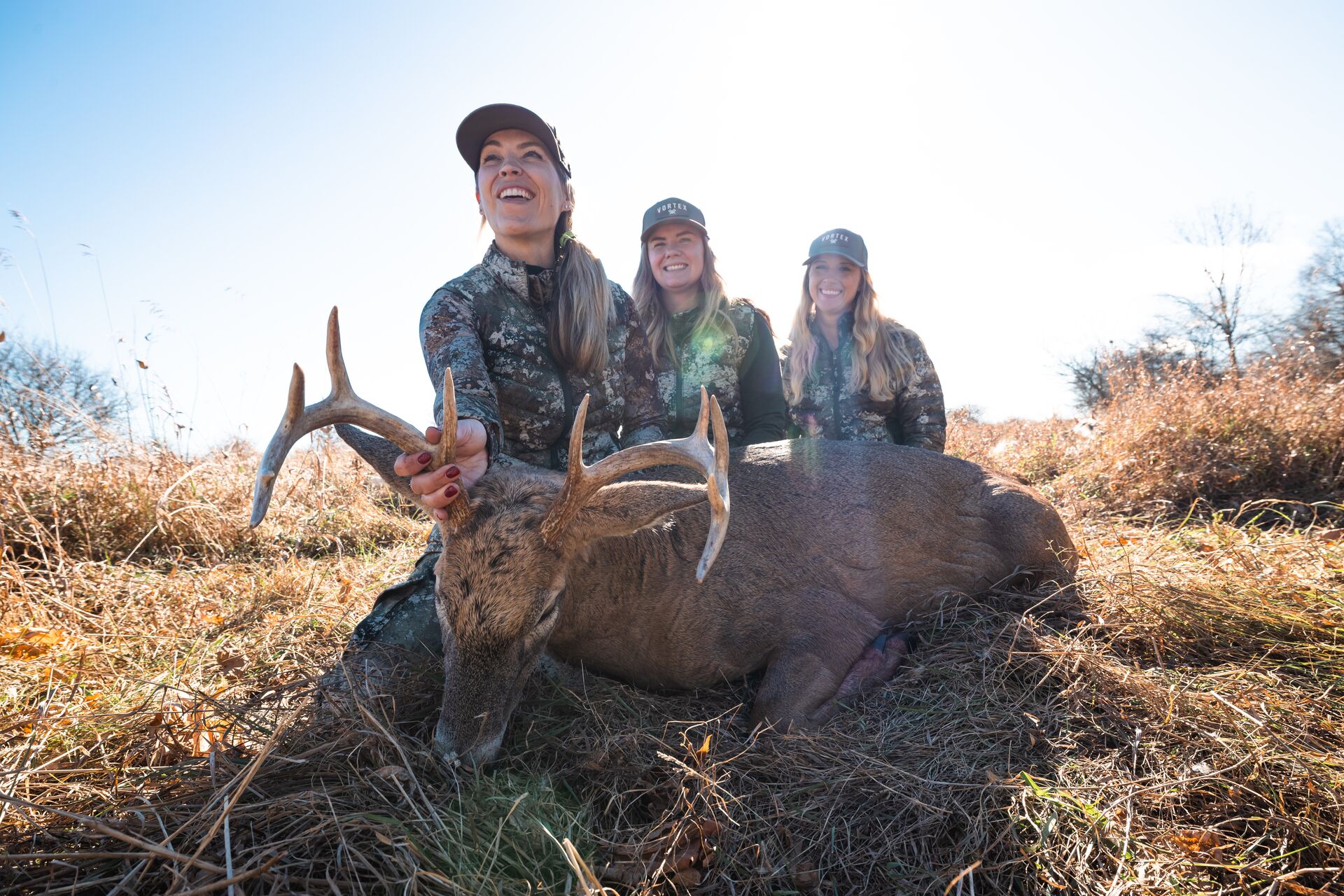 Three female hunters smile with deer after hunt. 