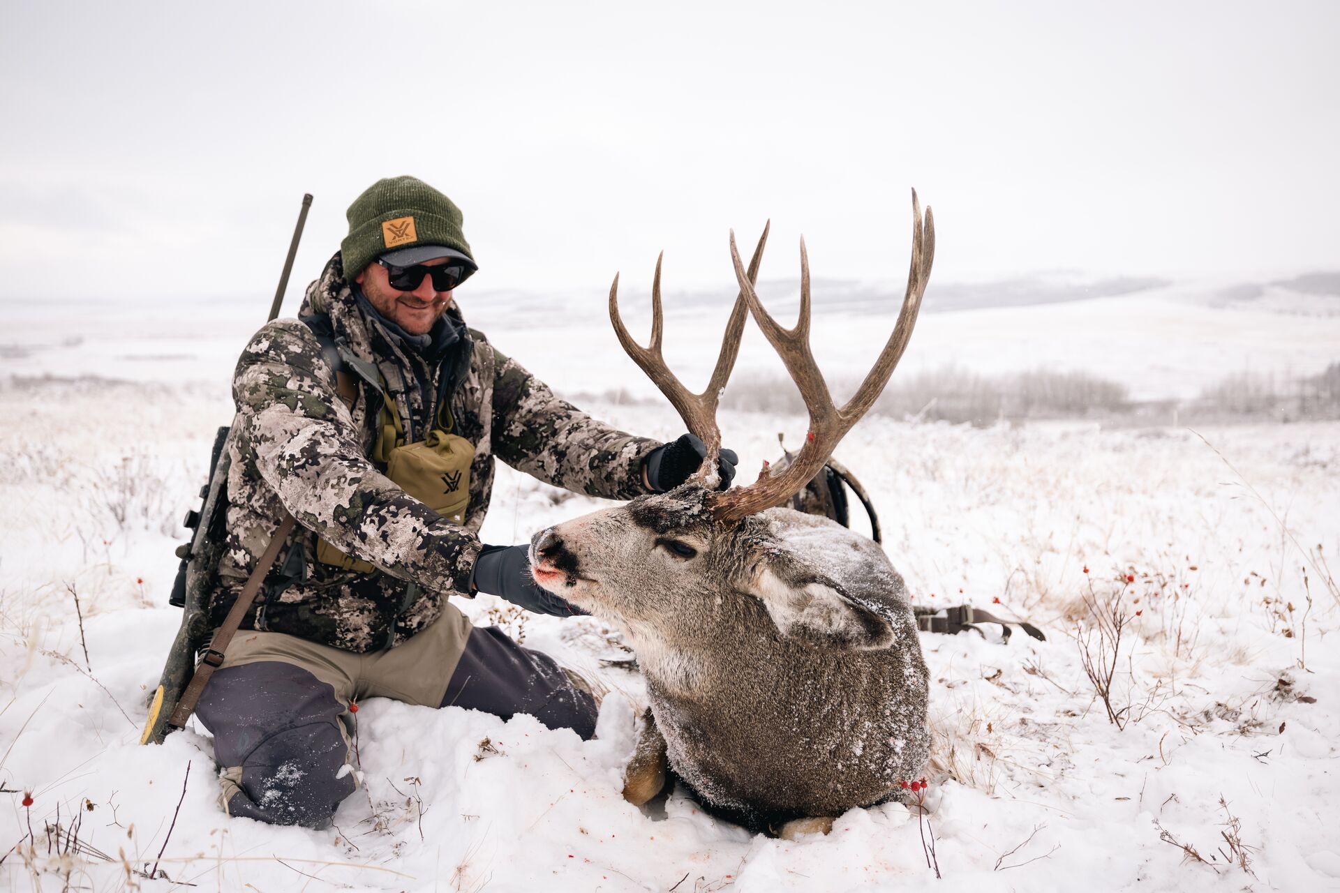 Hunter with rifle and buck deer in the snow after hunt. 