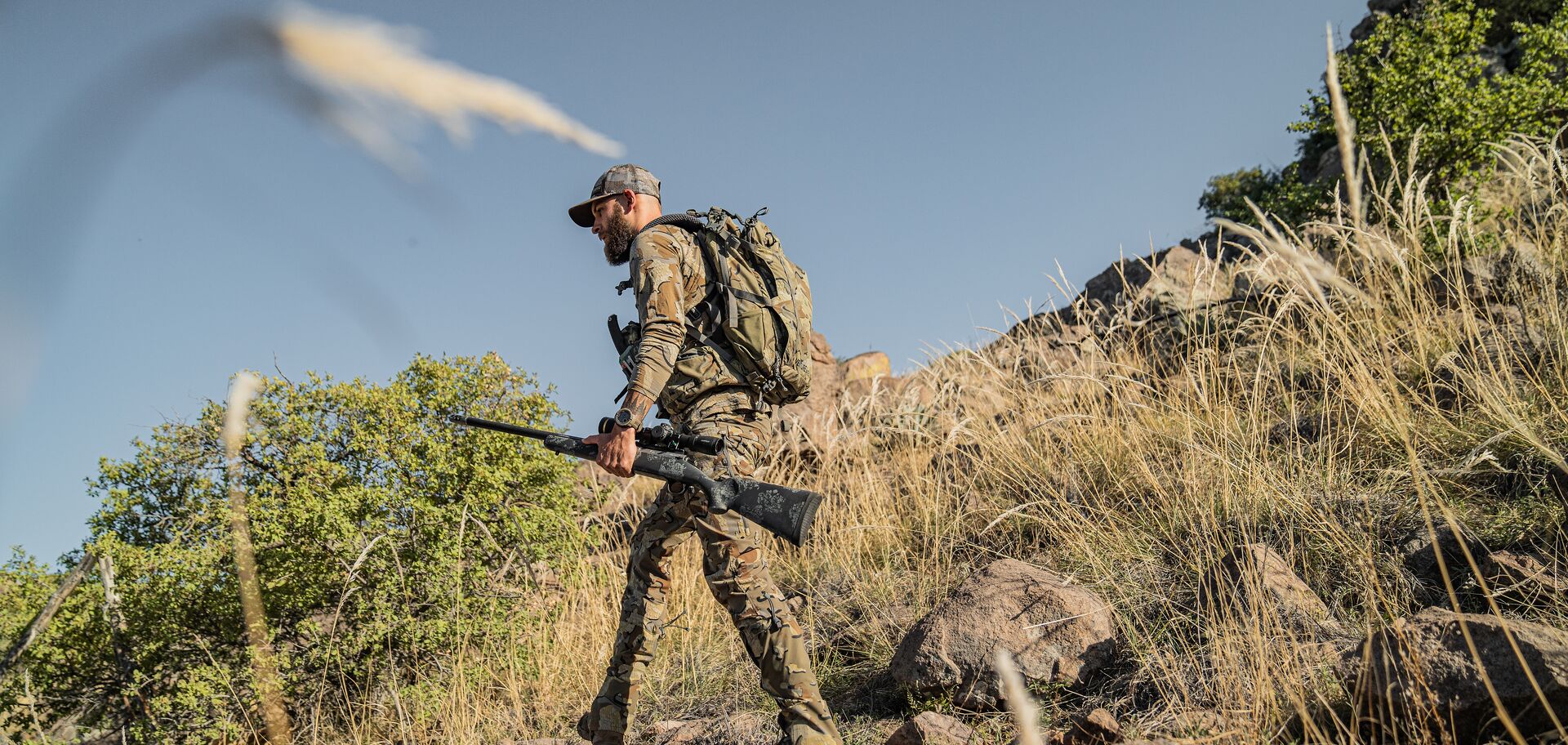 Hunter with gear and rifle hikes hill, Arizona mule deer hunting public land concept.
