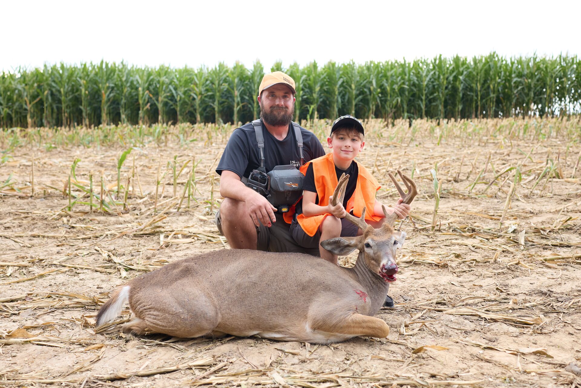 Man and boy wearing blaze orange pose with deer after hunt, New Jersey hunter safety course concept. 