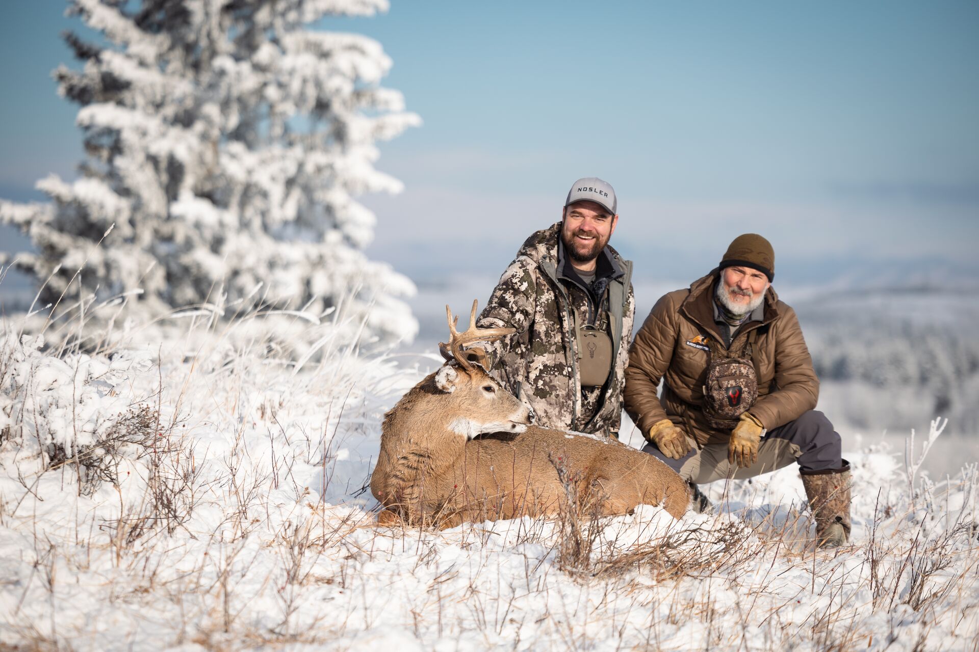 Two hunters in the snow with buck deer after hunt. 