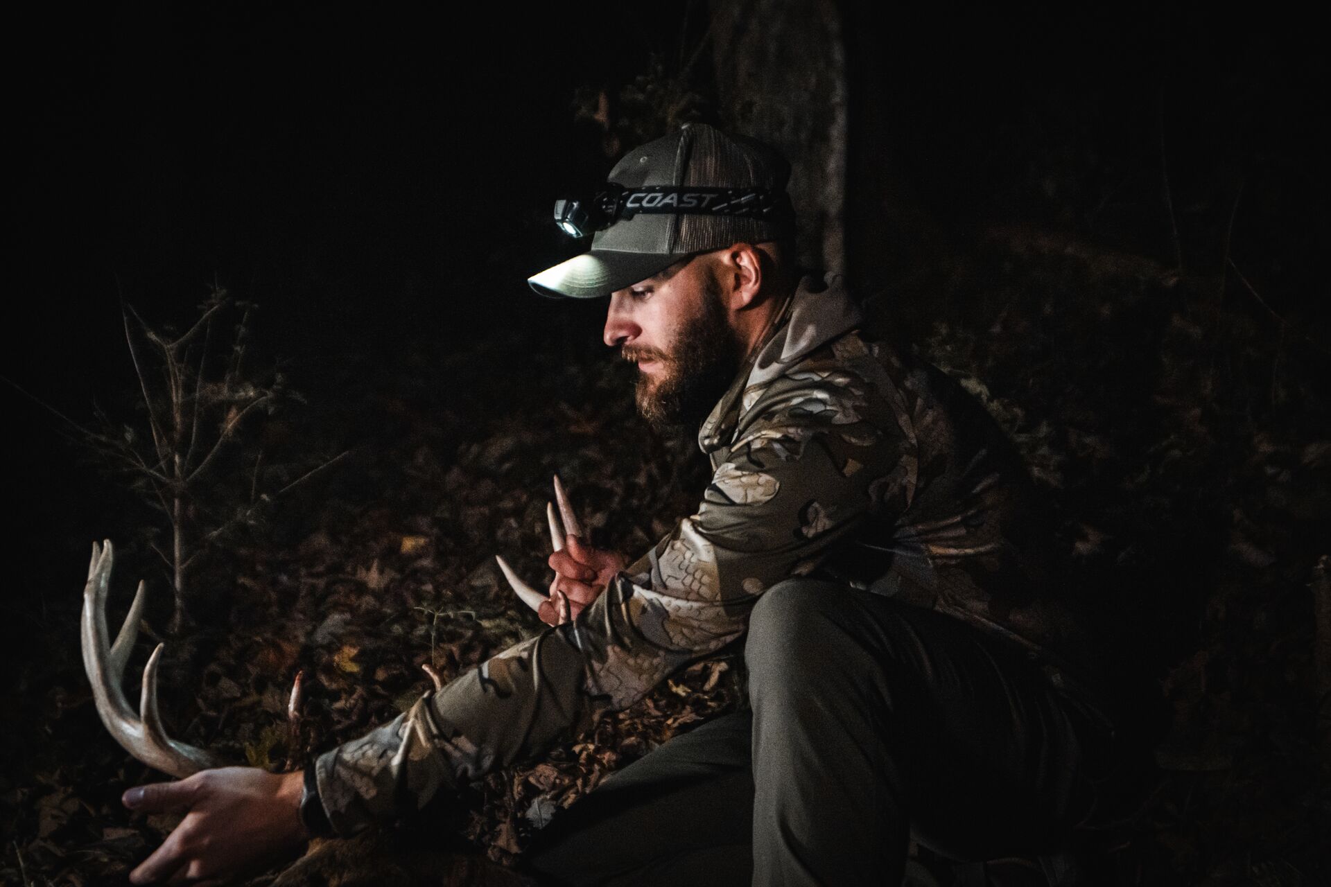 Hunter in the dark with headlamp and buck on ground, deer hunting for beginners concept.