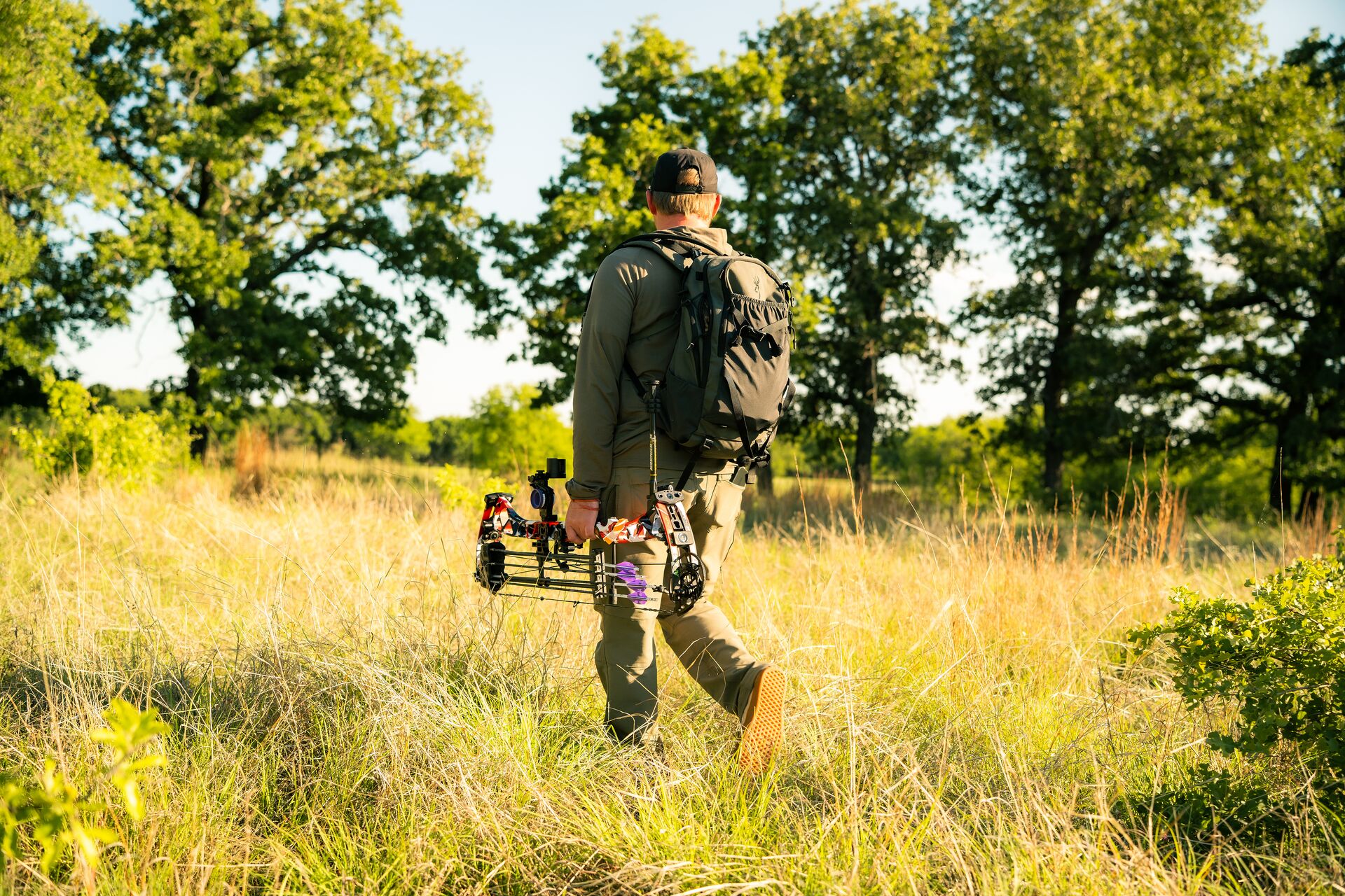 Hunter with bow and gear walks in a field, get an Indiana hunting license concept. 