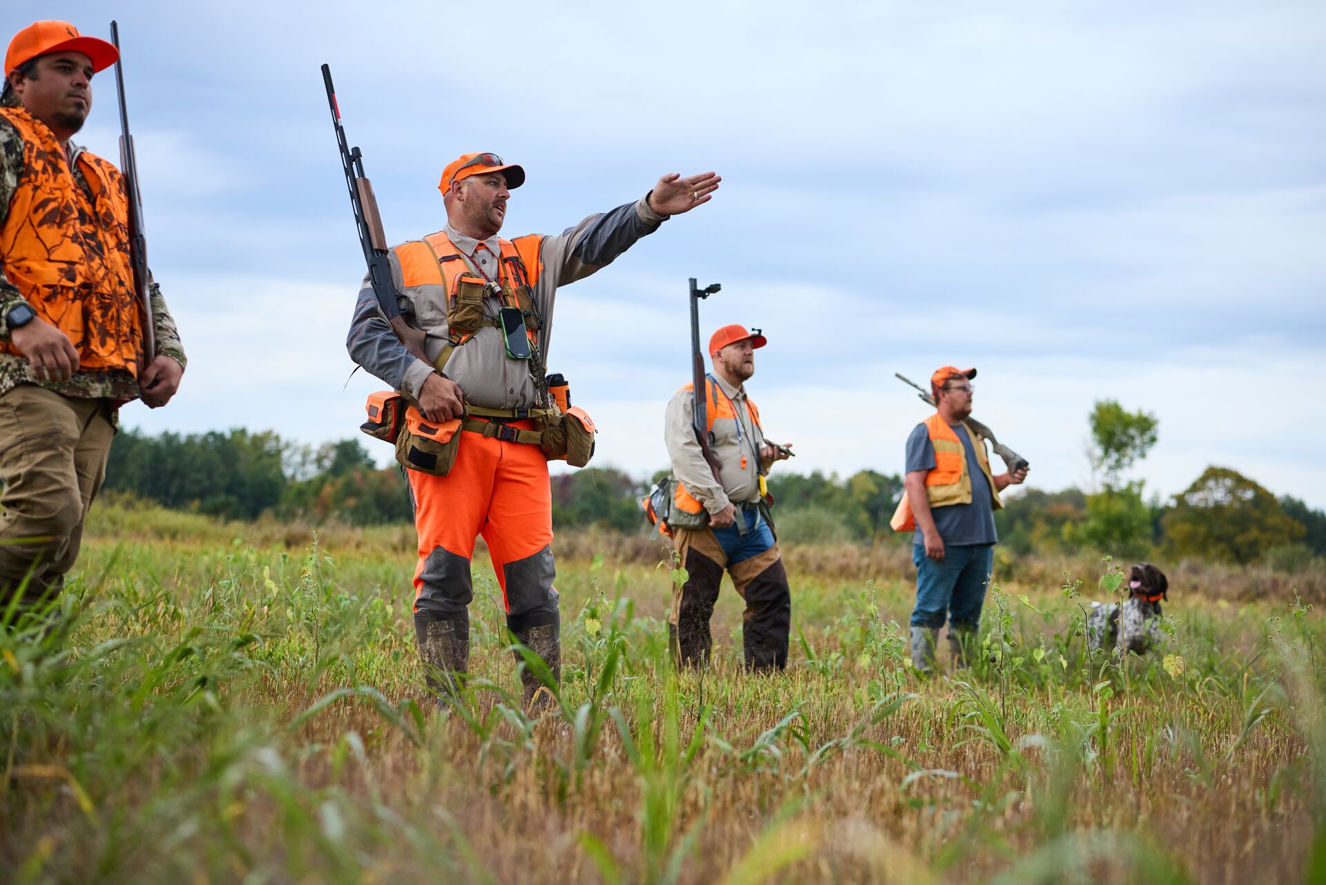 Several hunters in blaze orange with dog for upland game hunt. 