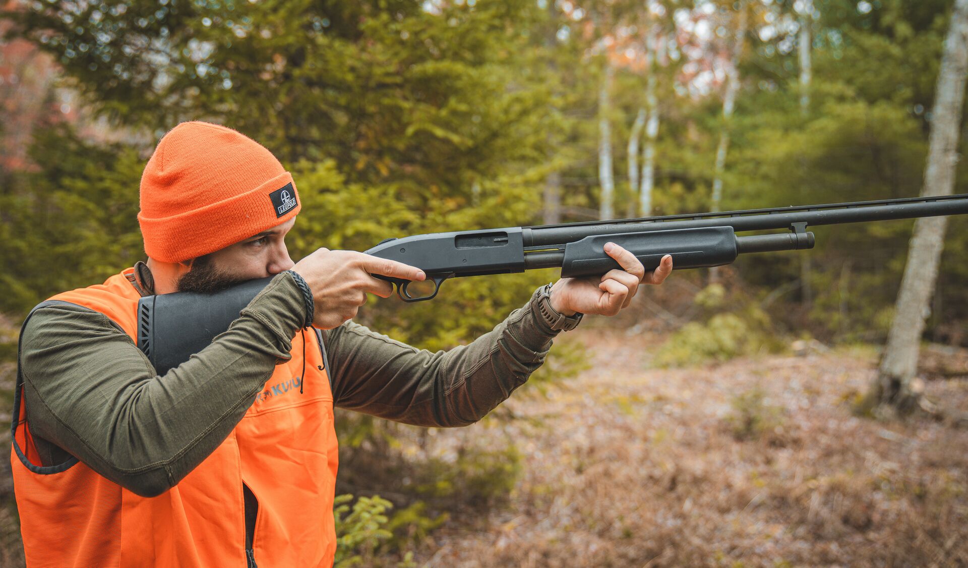 Hunter in blaze orange aims a shotgun, how to get an RI hunting license concept. 