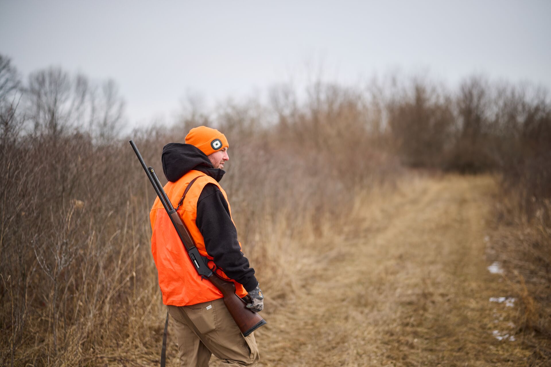 Hunter in blaze orange with firearm walks path, Wisconsin hunting license cost concept. 