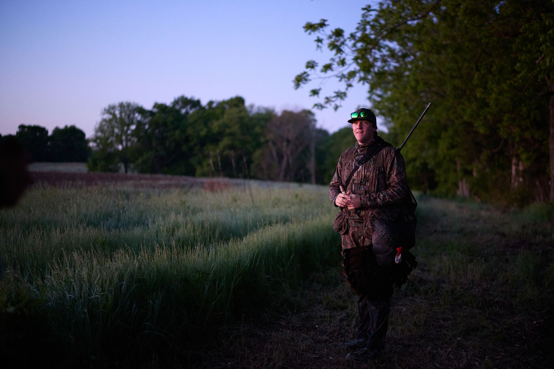 Hunter using turkey call at edge of field, Michigan hunting license cost concept.