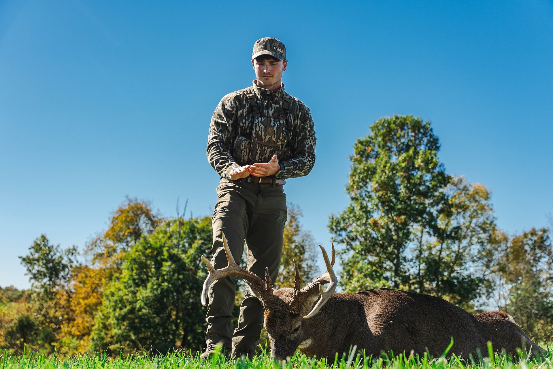Hunter stands over buck deer after hunt, Oklahoma hunting license cost concept. 