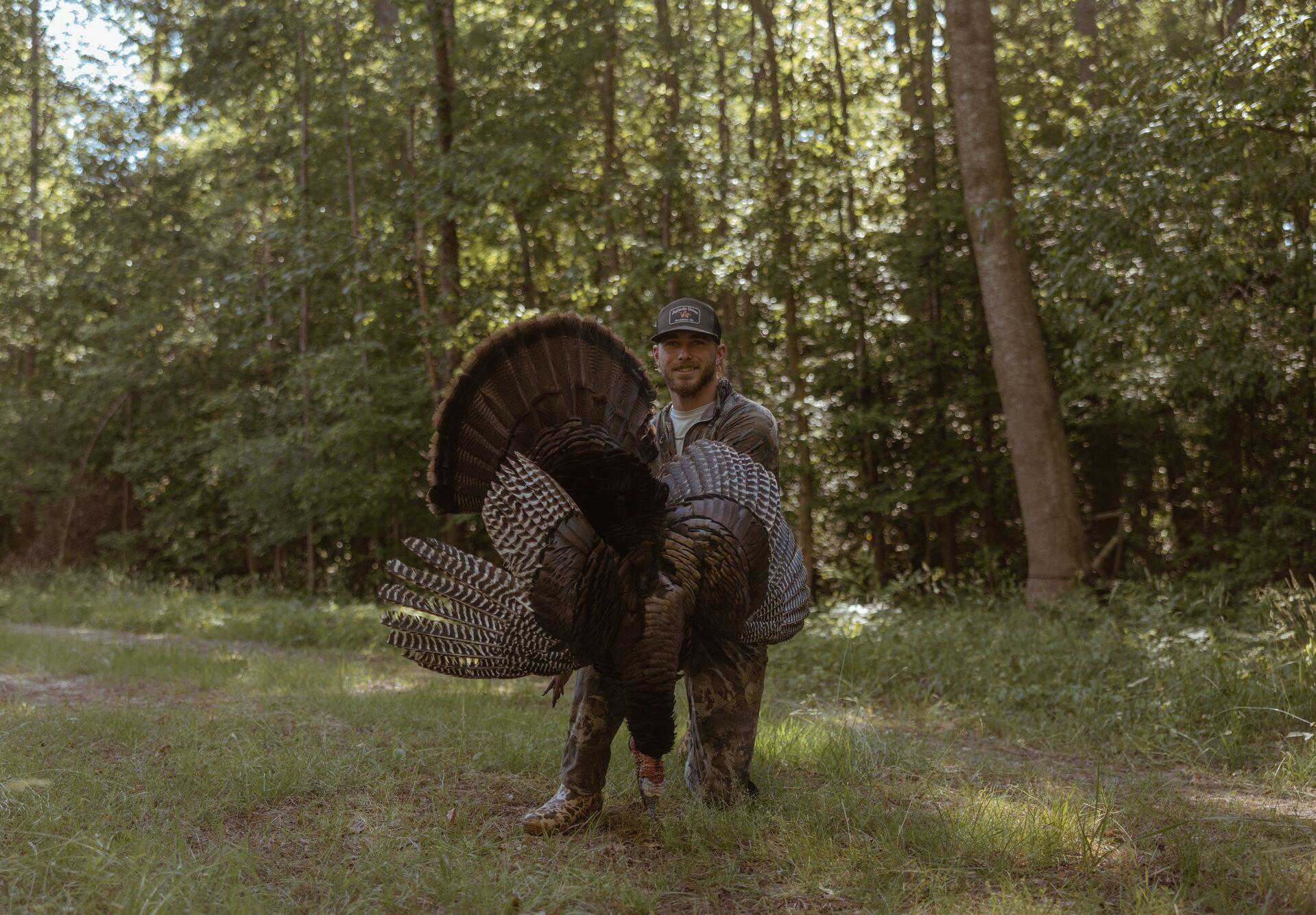 Hunter smiles and kneels while holding turkey after hunt.