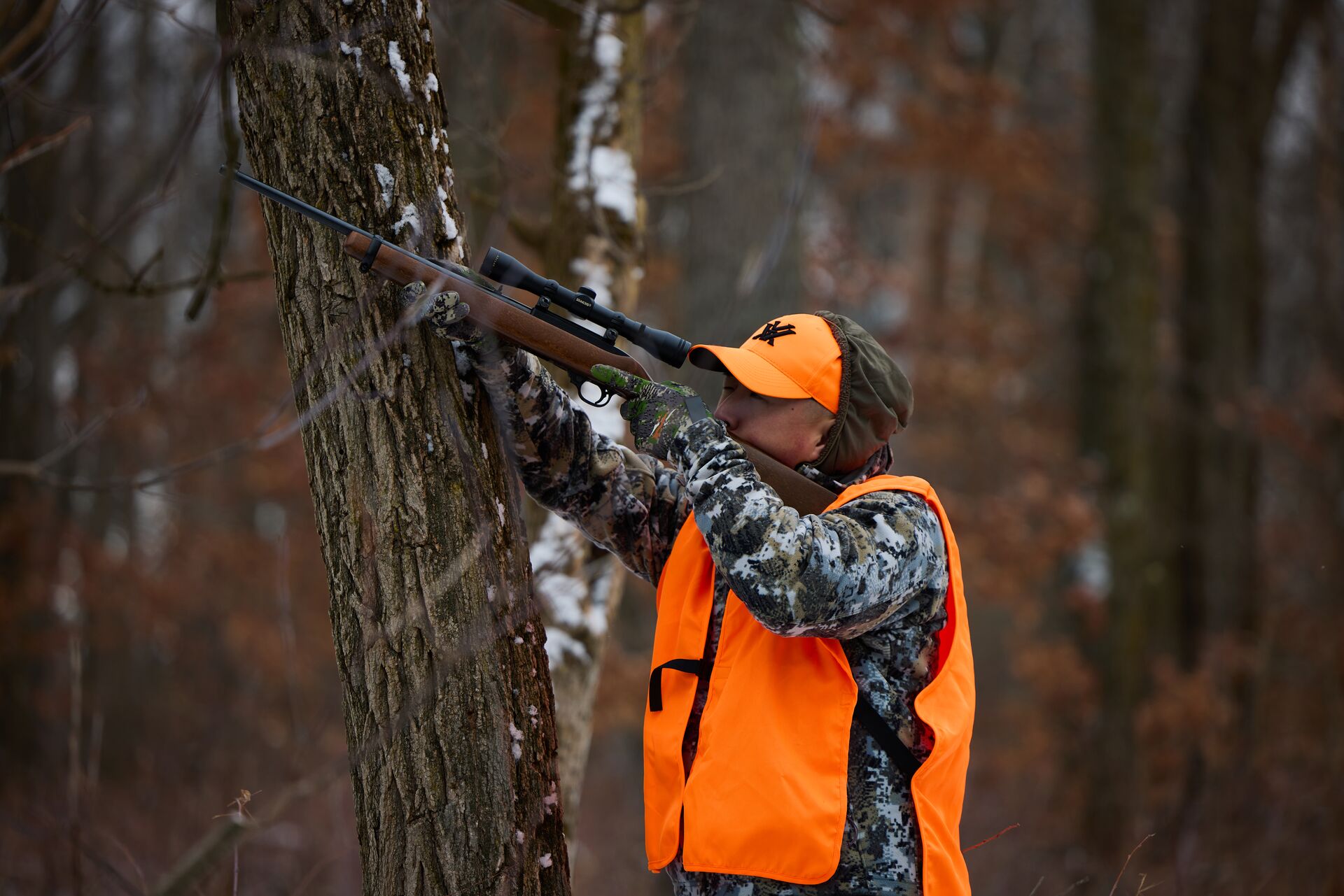 Hunter in blaze orange vest and hat aims firearm, Alabama hunting license concept.