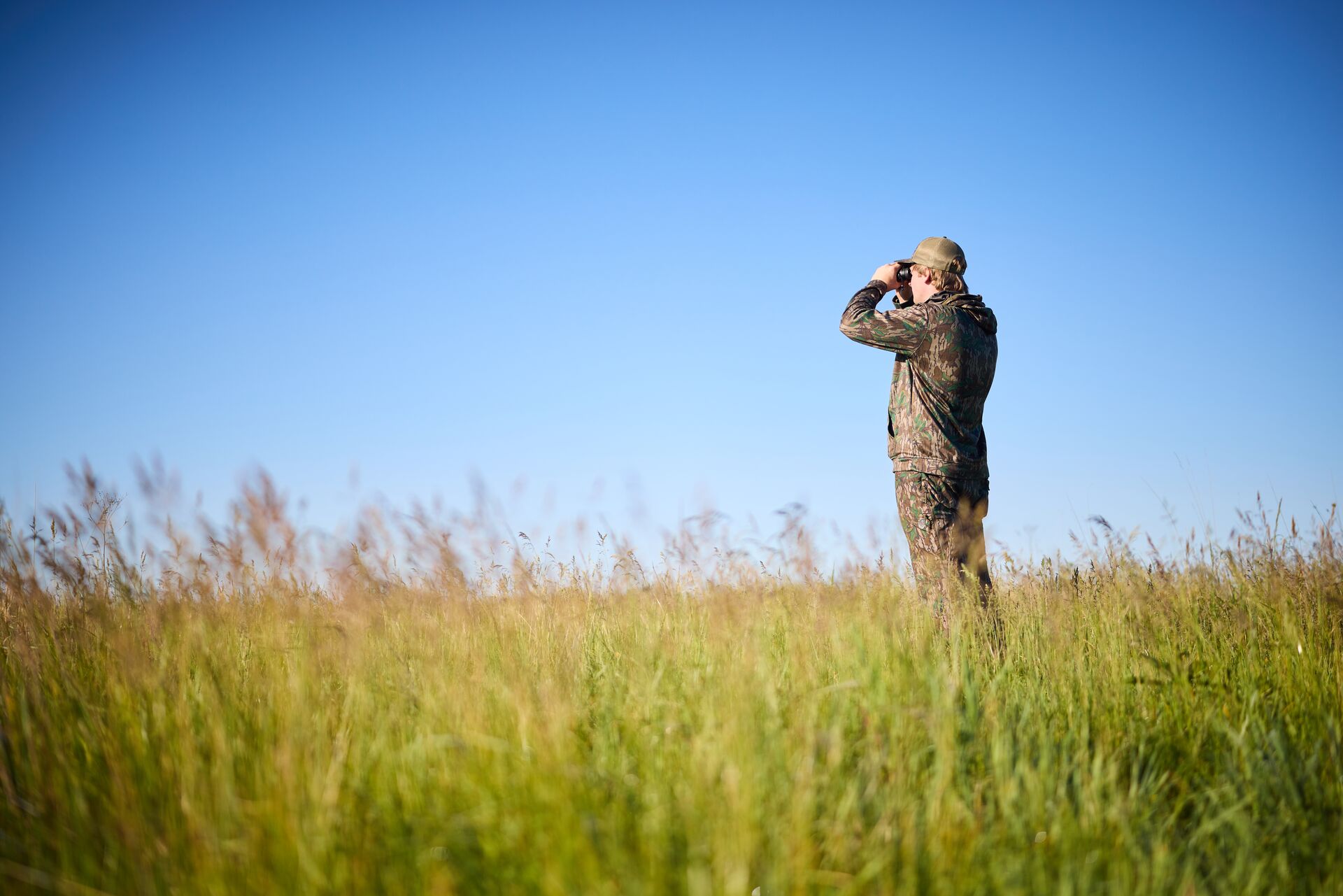 Hunter in field using binoculars, how much does an Alabama hunting license cost concept.