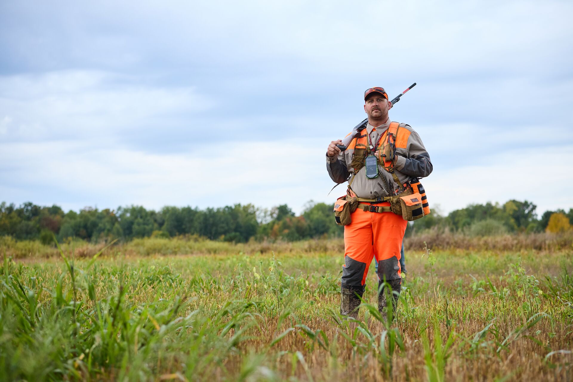 Hunter in blaze orange with gear for upland bird hunt, Iowa hunting license cost concept.