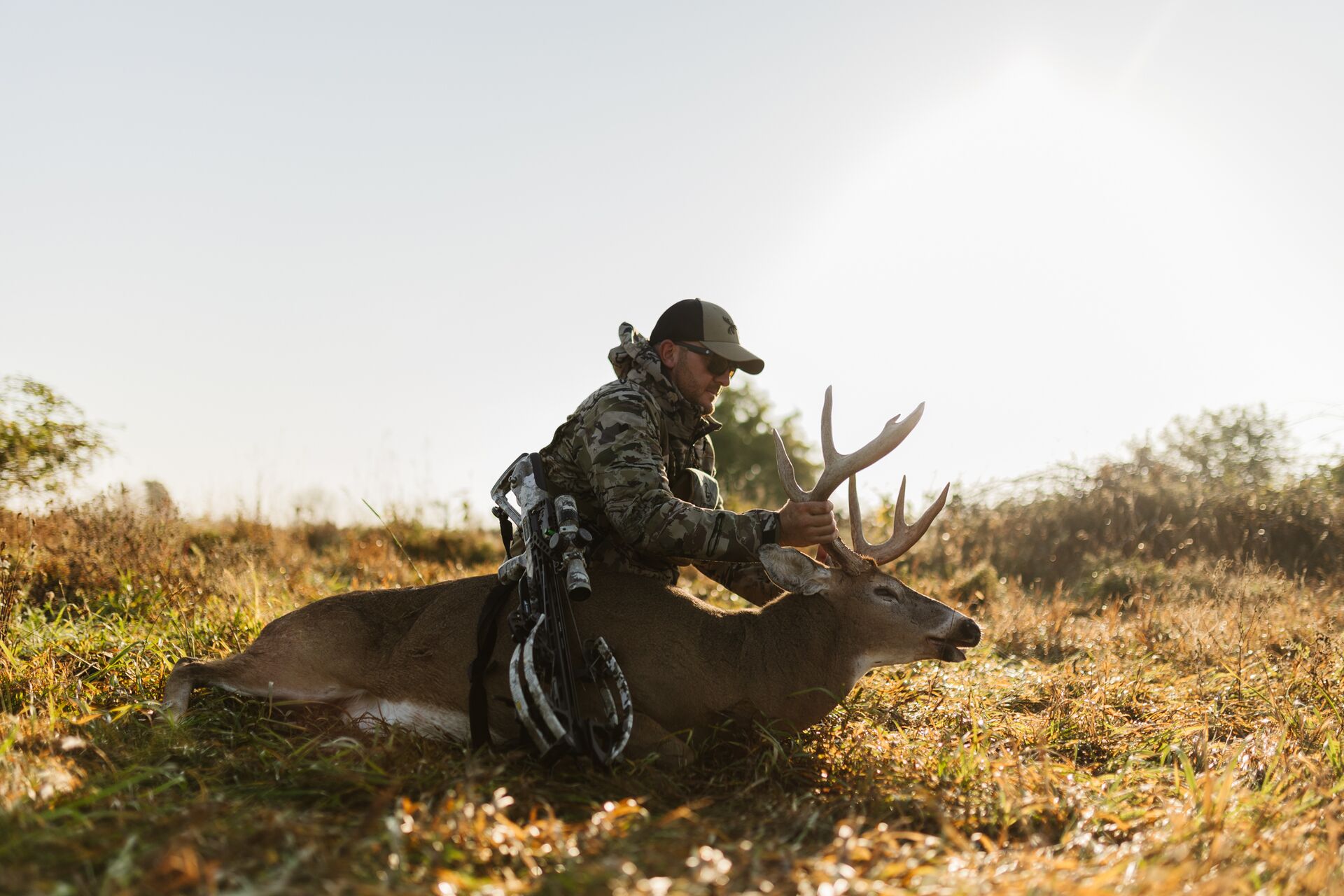 Hunter sits with buck deer on the ground holding antlers, how much does an Iowa hunting license cost concept. 