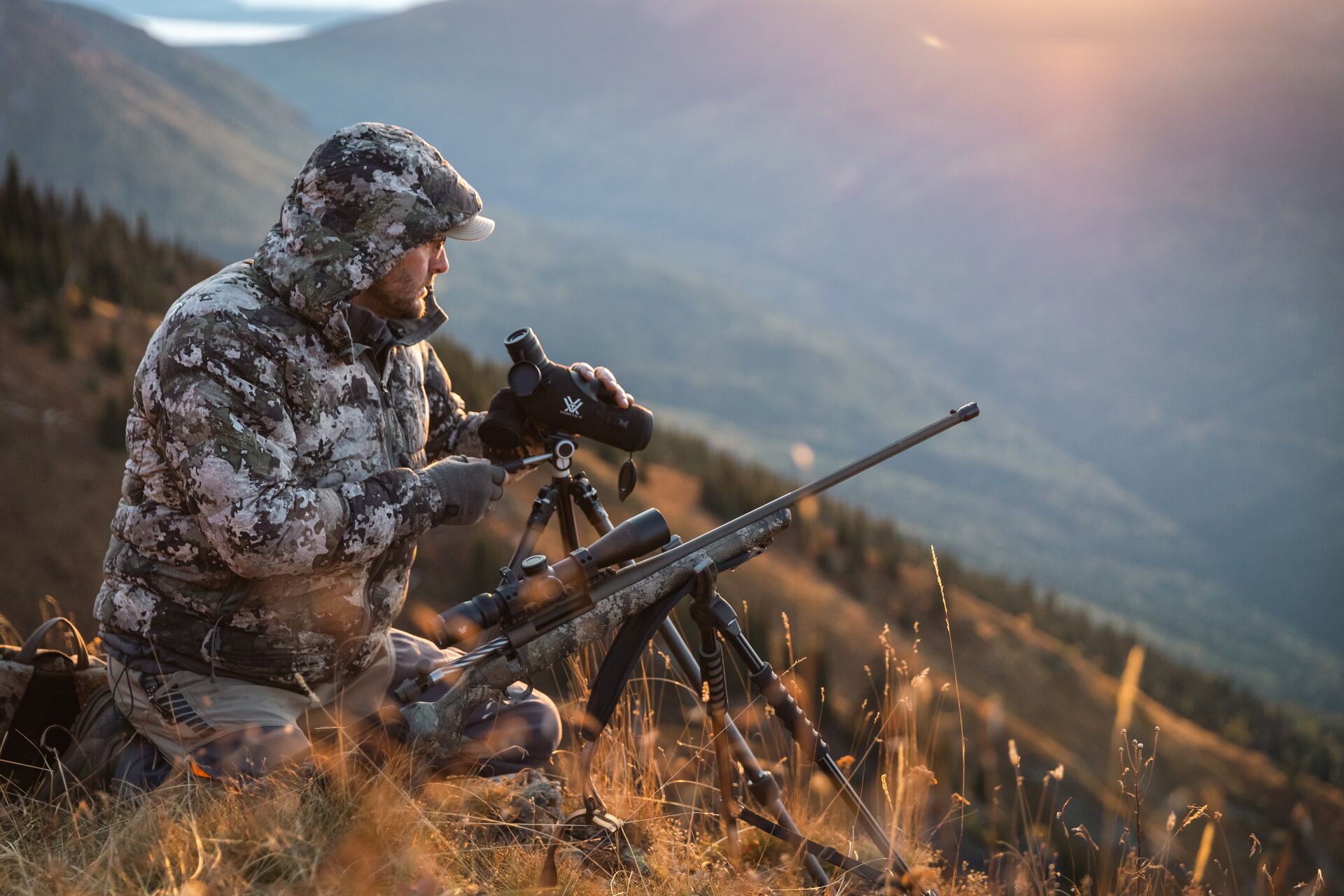 Hunter on a hill using scope for glassing, Wyoming hunting license cost concept.