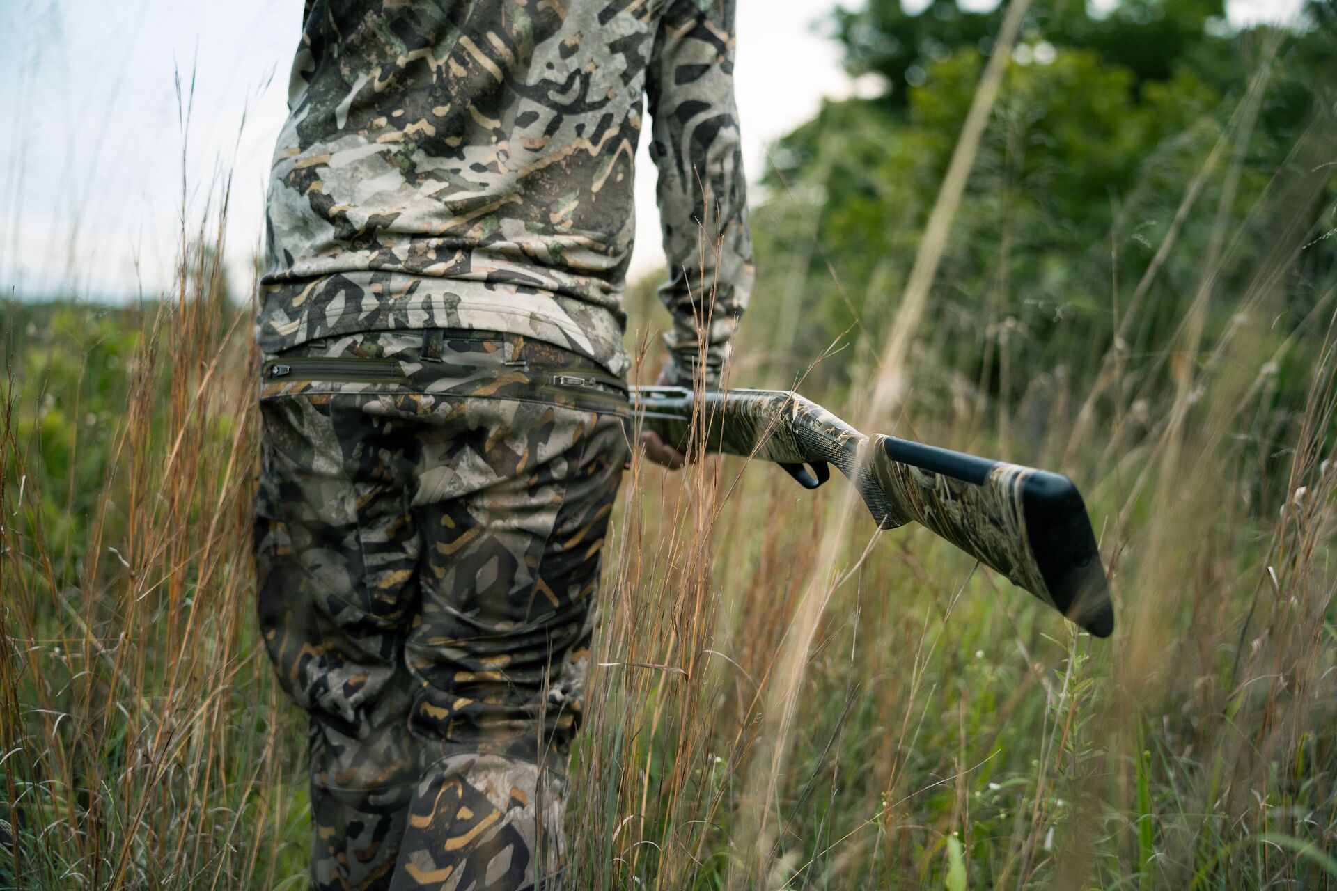 Back view of hunter in camo carrying firearm, Louisiana hunting license cost concept.