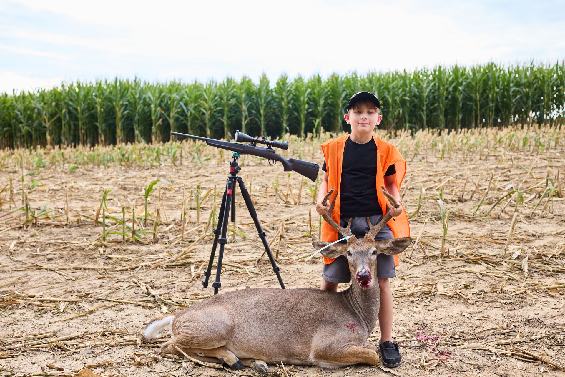 Boy in orange vest poses with buck deer after hunt, do you need a hunting license concept. 