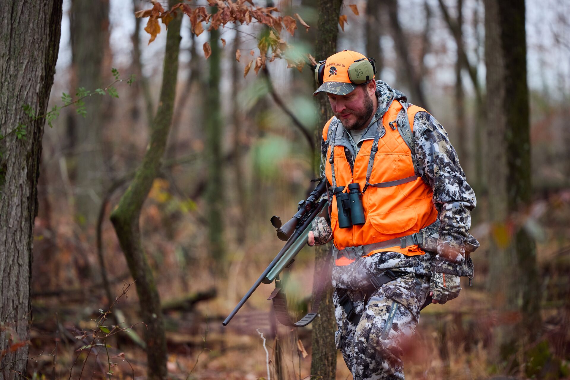 Hunter in camo and blaze orange with firearm in the woods, hunting license cost concept. 