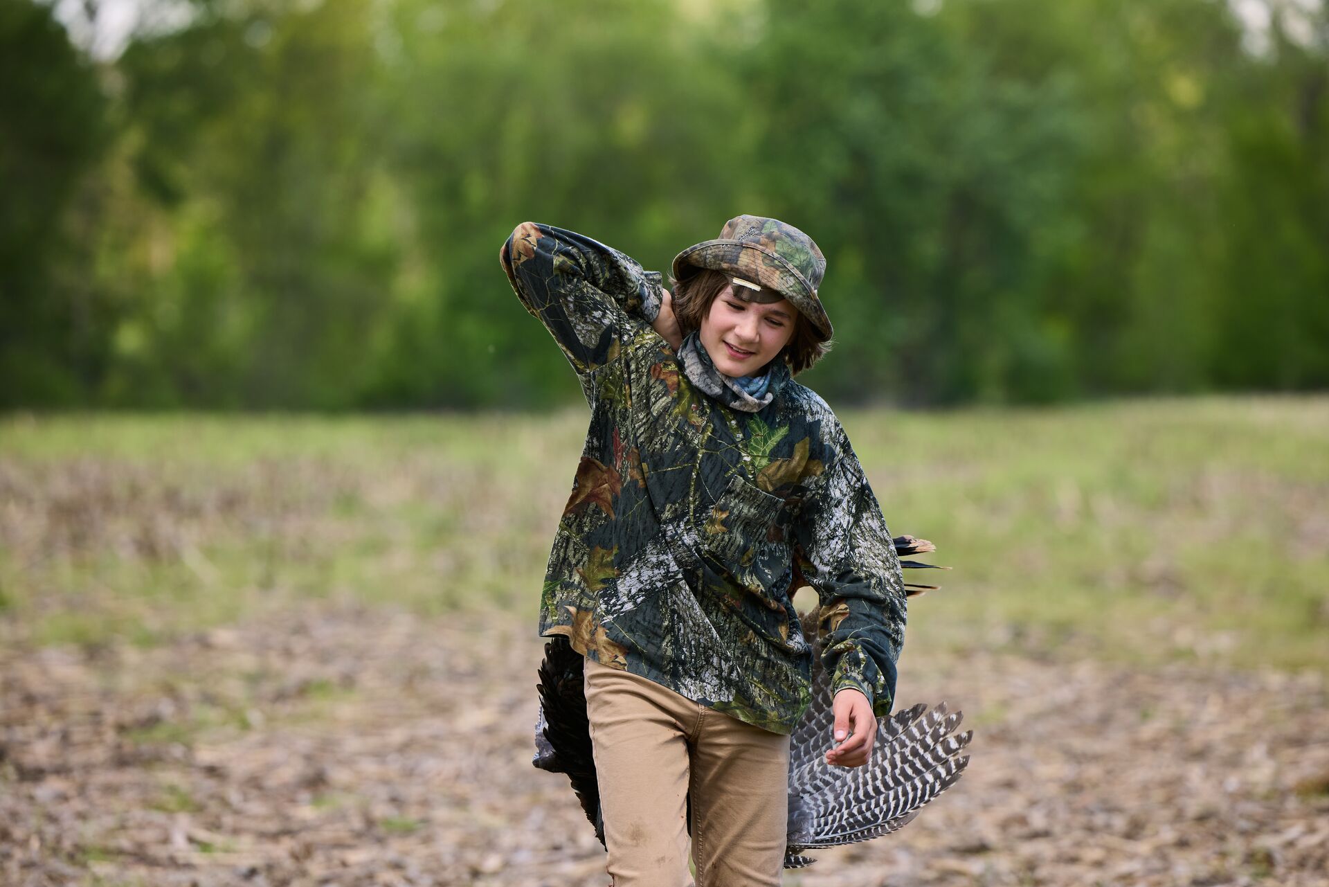 Boy in camo carries turkey after hunt, hunting license Ohio concept. 