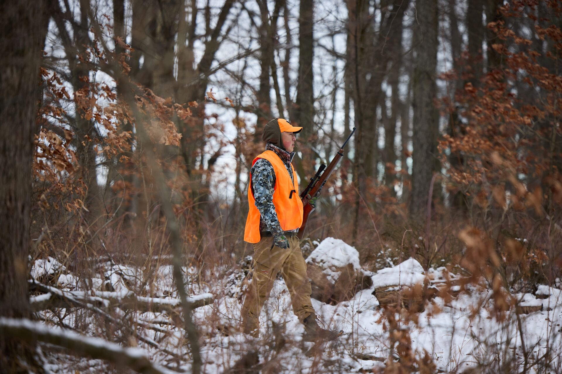 Hunter in blaze orange walks in woods, take a hunter safety course concept.