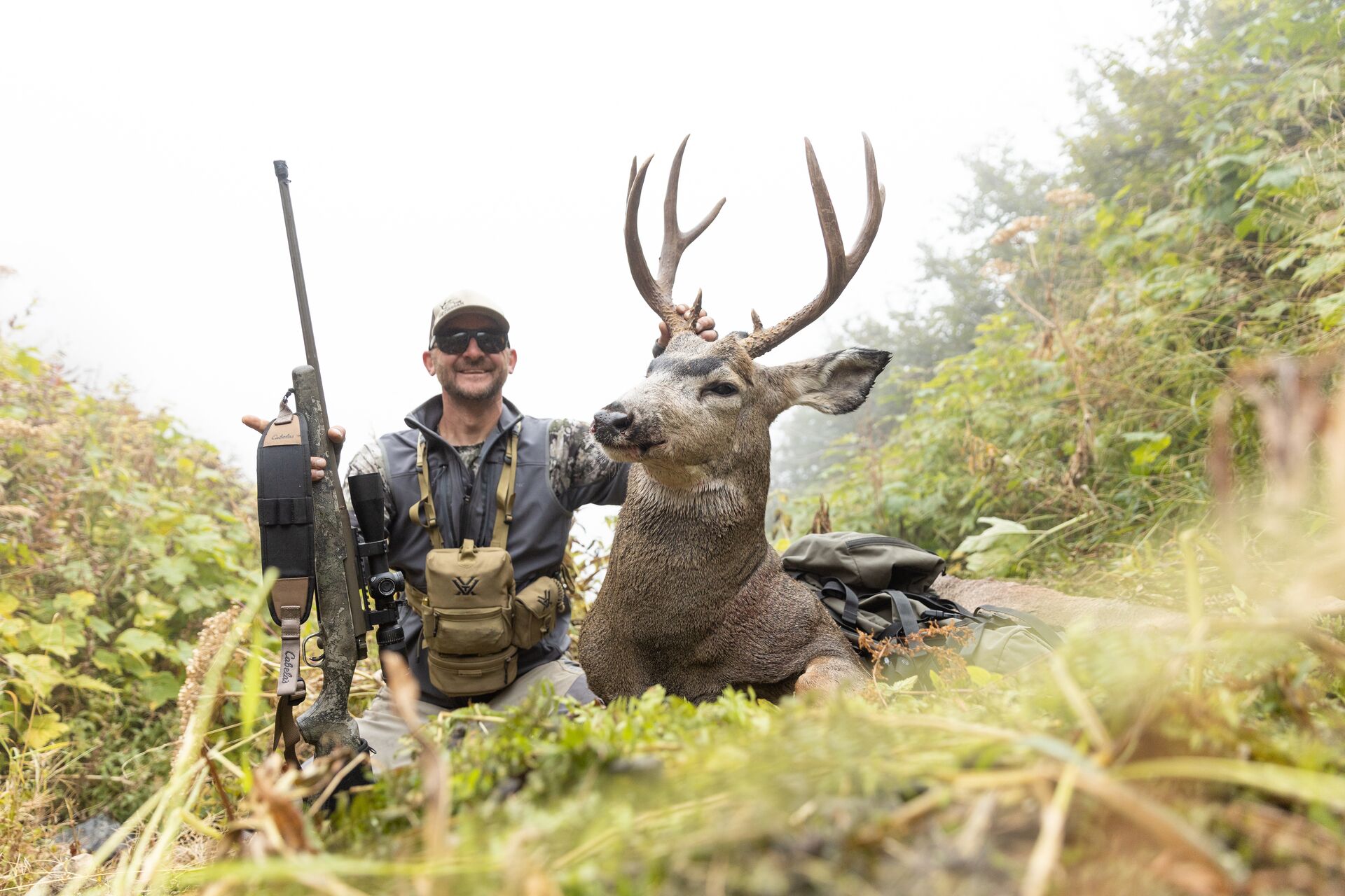 Smiling hunter with large mule deer and rifle after hunt, hunting license and tags concept.