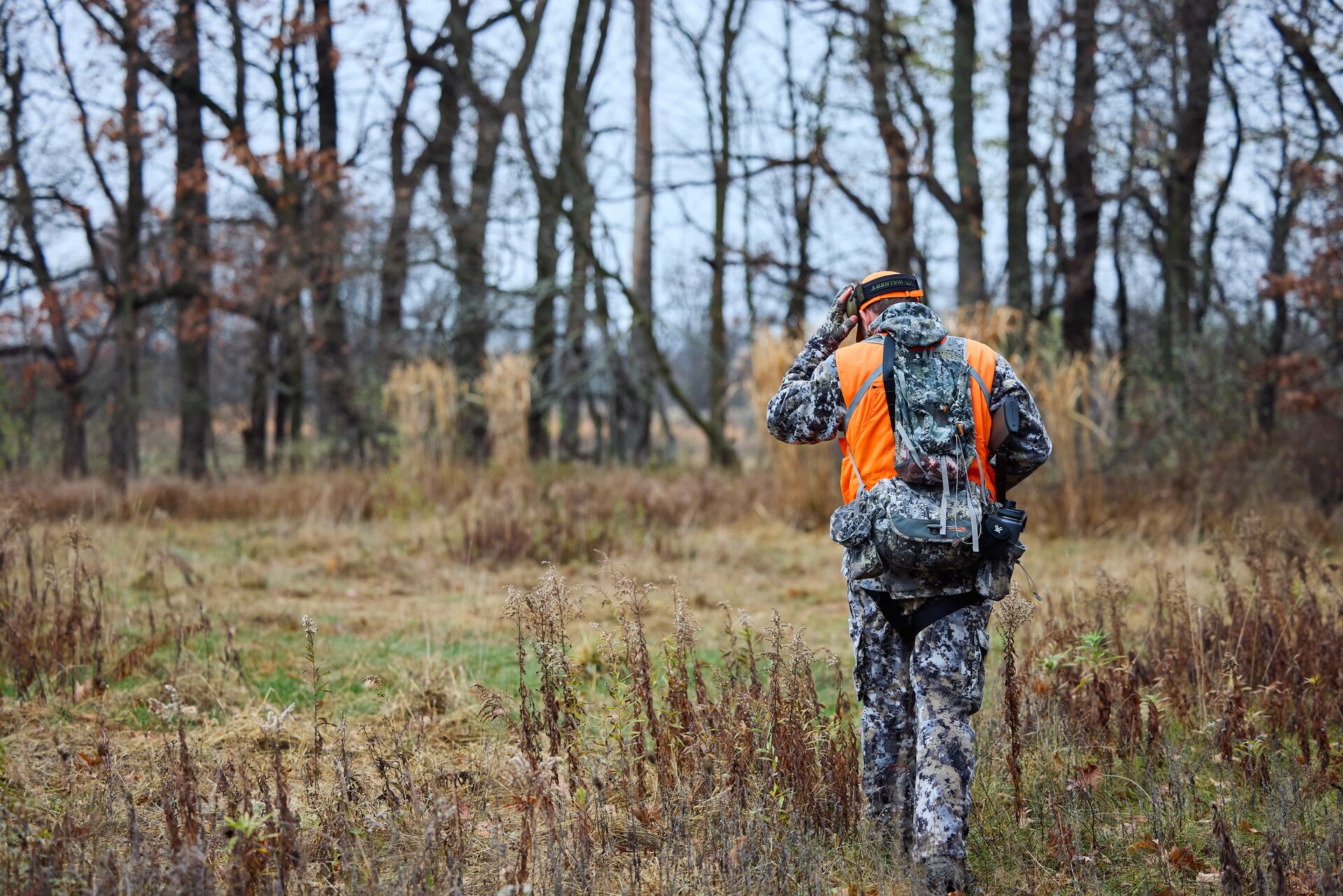 Hunter in camo and blaze orange walks away, how much does an Illinois hunting license cost concept.