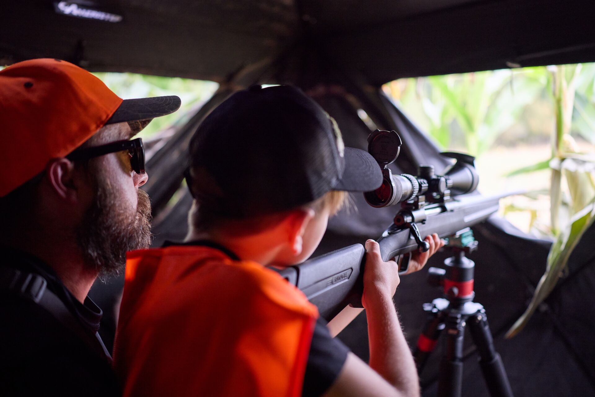 Man with boy aiming rifle in hunting blind, junior hunting license concept.