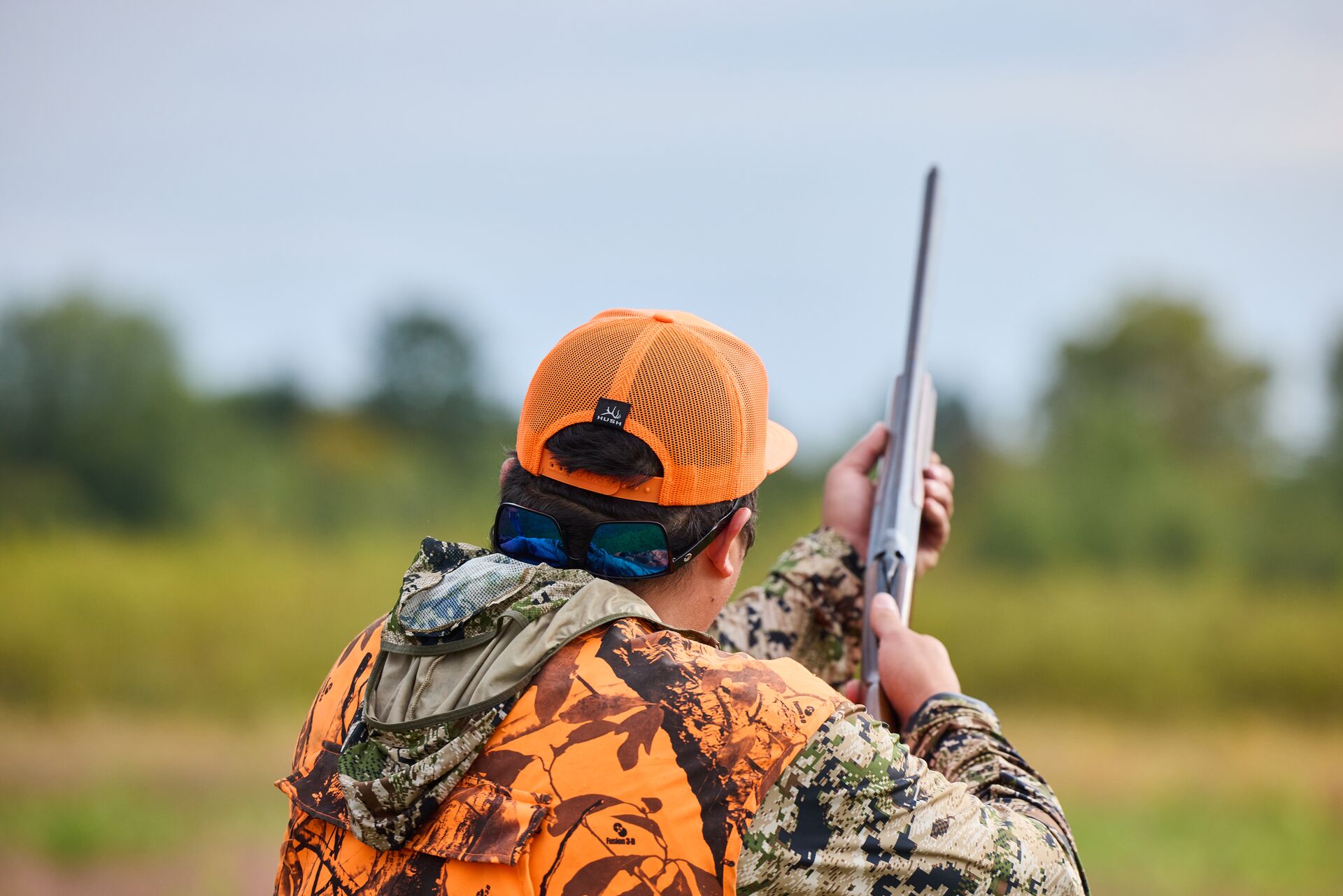 Back view of hunter in orange with shotgun for upland hunt, get a TX hunting license concept.