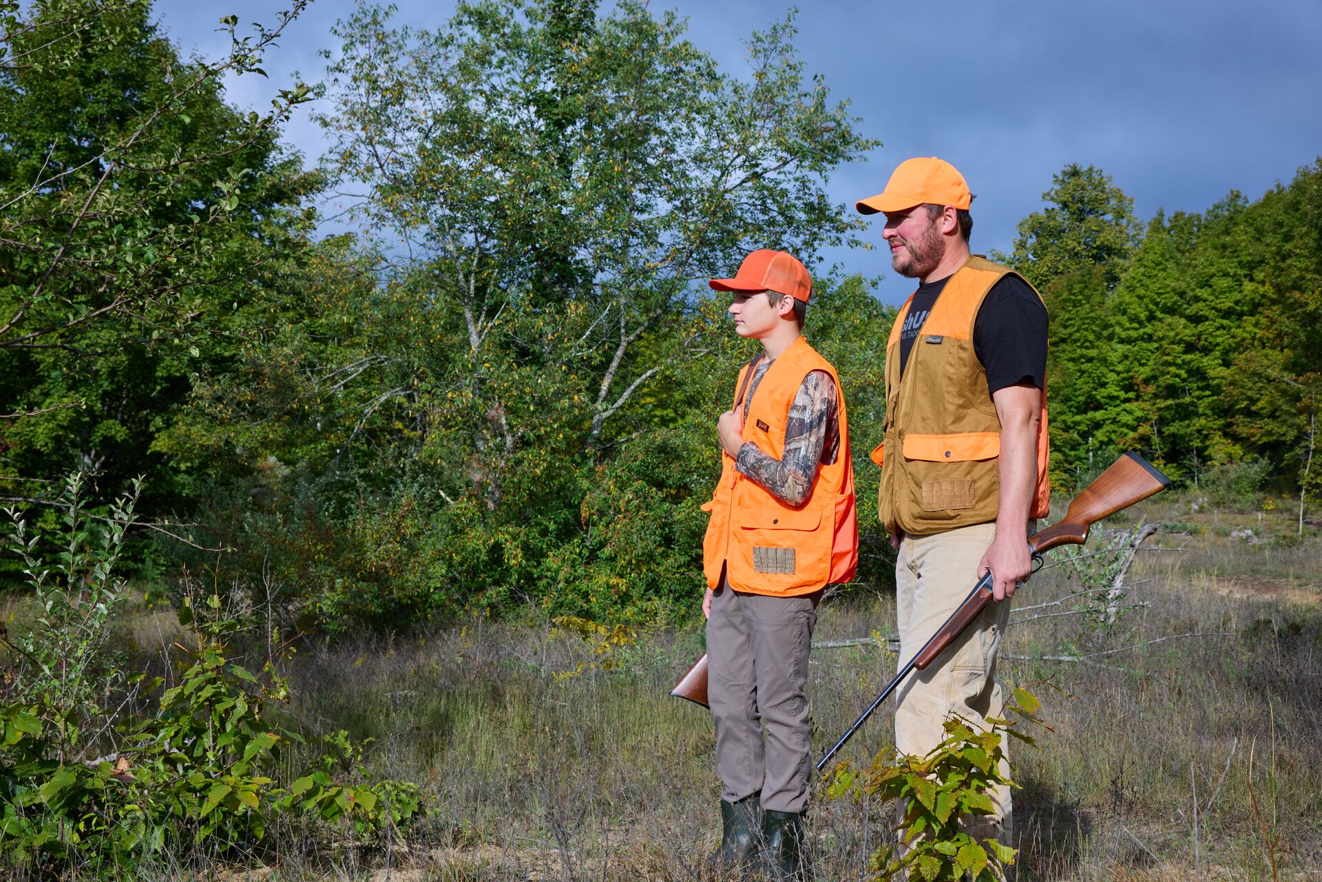 Boy and man in blaze orange with firearms, how to prepare for hunter education field day concept.