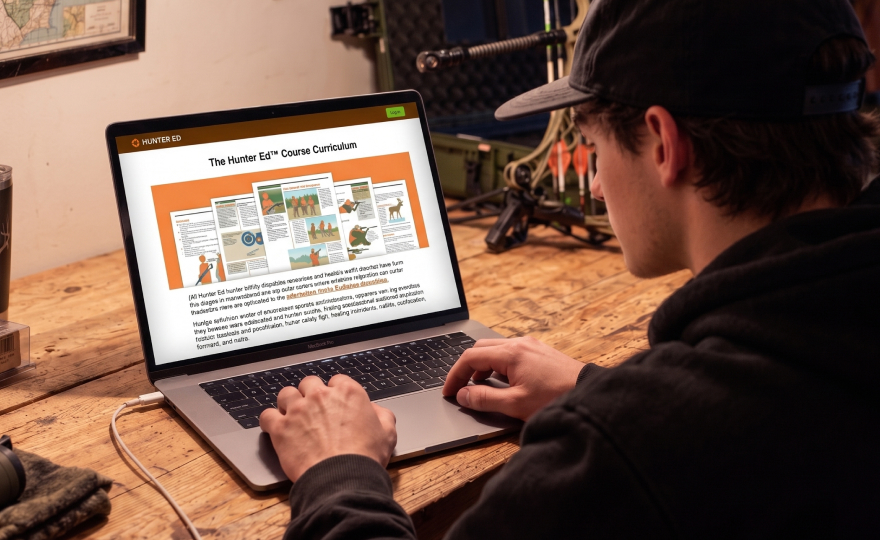 Hunter using laptop with Hunter-Ed onscreen, hunter safety course online concept.