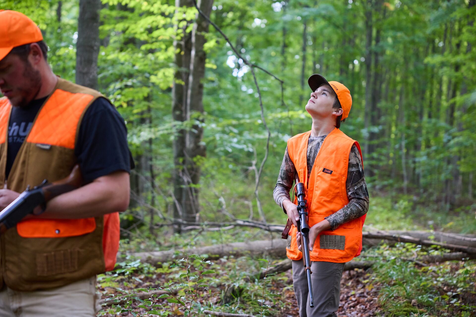 Boy and man in hunter orange with shotguns in woods, hunter education field day concept. 
