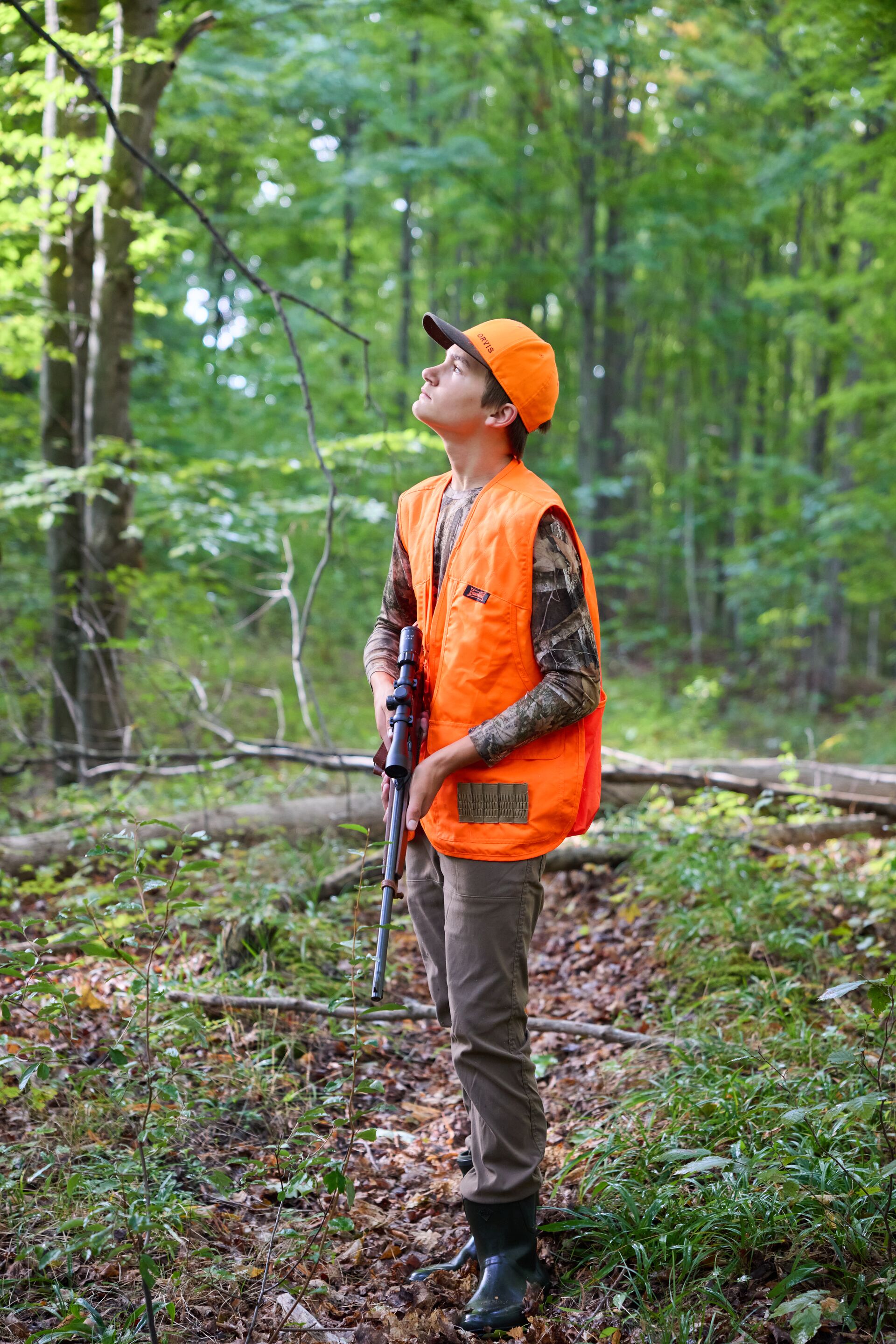 Boy in blaze orange hat and vest with firearm, youth hunting license age concept.